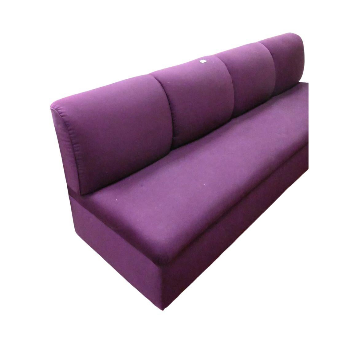 Banqueta tapizada en color berenjena, con respaldo ajustado de cuatro cojines y asiento corrido.  Se asienta sobre una base cromada.  Manchas en el tejido.