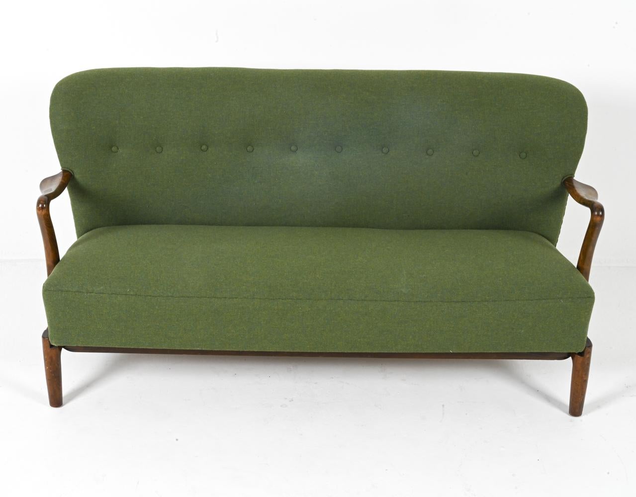 This elegant upholstered beech sofa was crafted by renowned furniture maker Alfred Christensen in the 1950s. This piece embodies the essence of Mid-Century Modernism, seamlessly blending smooth lines, warm beech wood, and inviting green