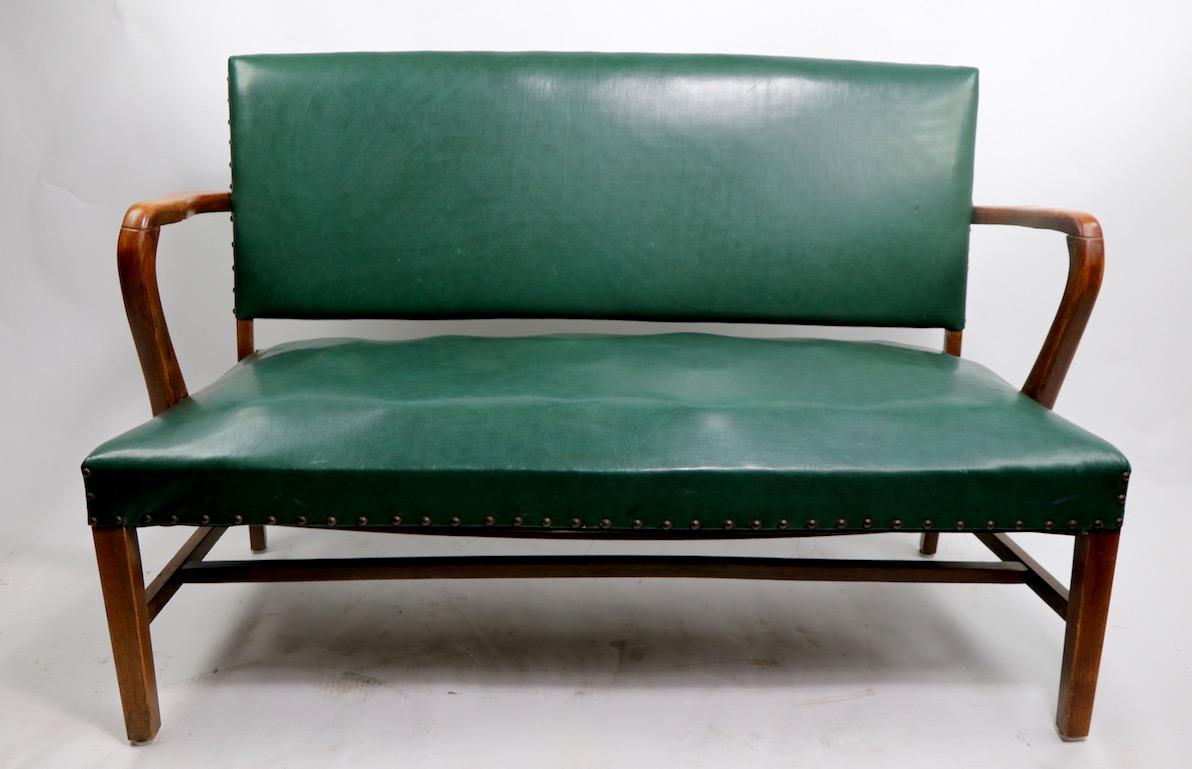 Stylish bench with upholstered seat, back, and curved wood arms. We have attributed the bench to Gunlocke, however it is unsigned. This example shows cosmetic wear, and will need to be reupholstered. In addition, the two stretchers are misshapen,