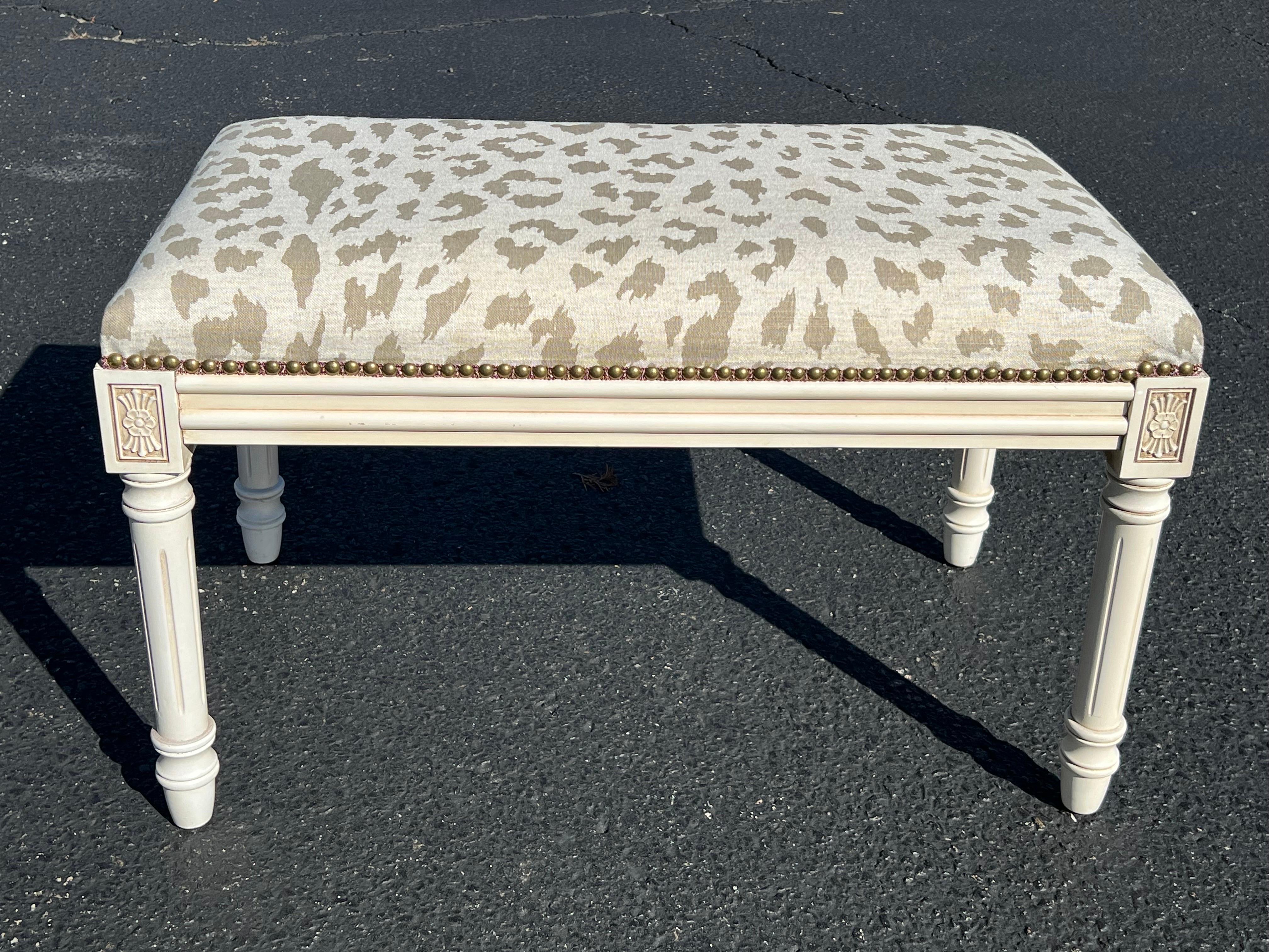 Upholstered bench with animal print upholstery. Nice cream painted stool base with brass beaded nails. Cream and tan animal print upholstery covers this traditional bench. Use at the foot of a bed or under a console.