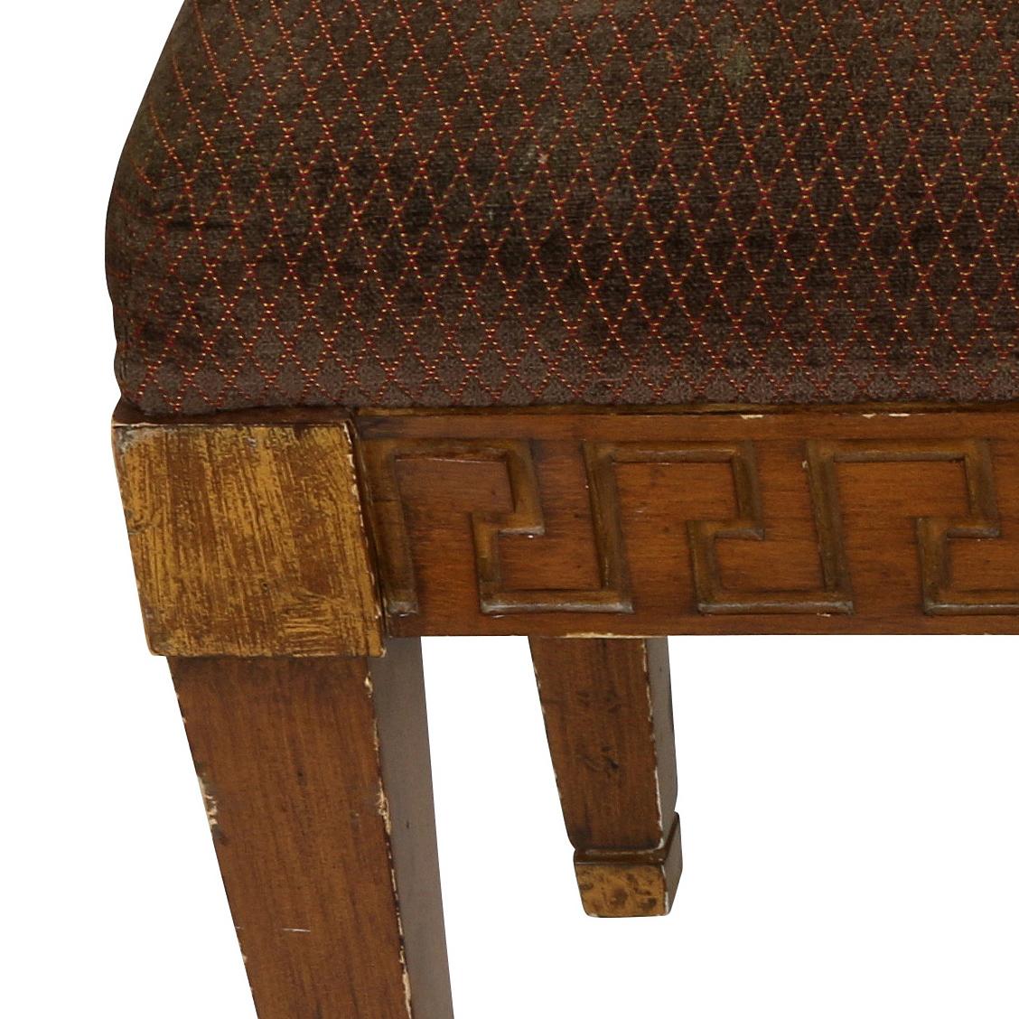 Vieux banc en bois avec un motif de clé grecque sculpté sur le tablier et tapissé de velours foncé à motif de treillis.