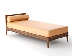 Cama de día tapizada con colchón y cojín decorativo sobre base y patas de madera