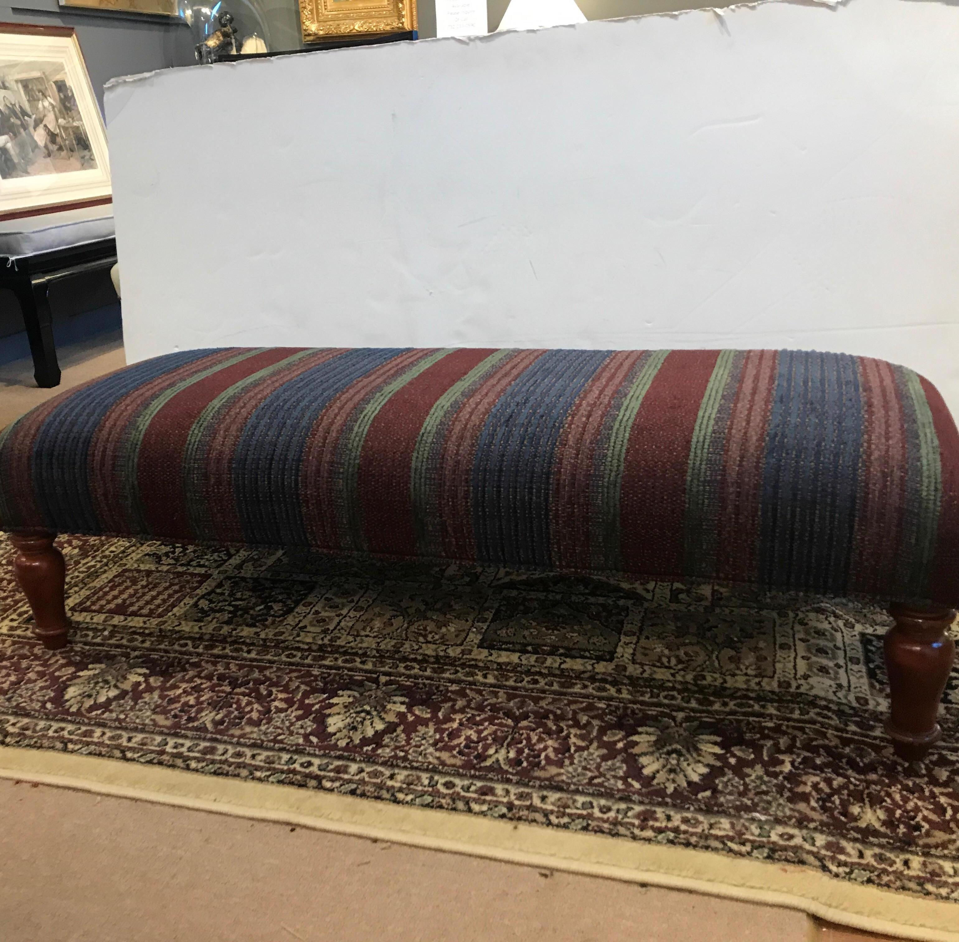 A long ottoman bench with sturdy turned legs covered in a vibrant woven chenille textured fabric with turned legs.