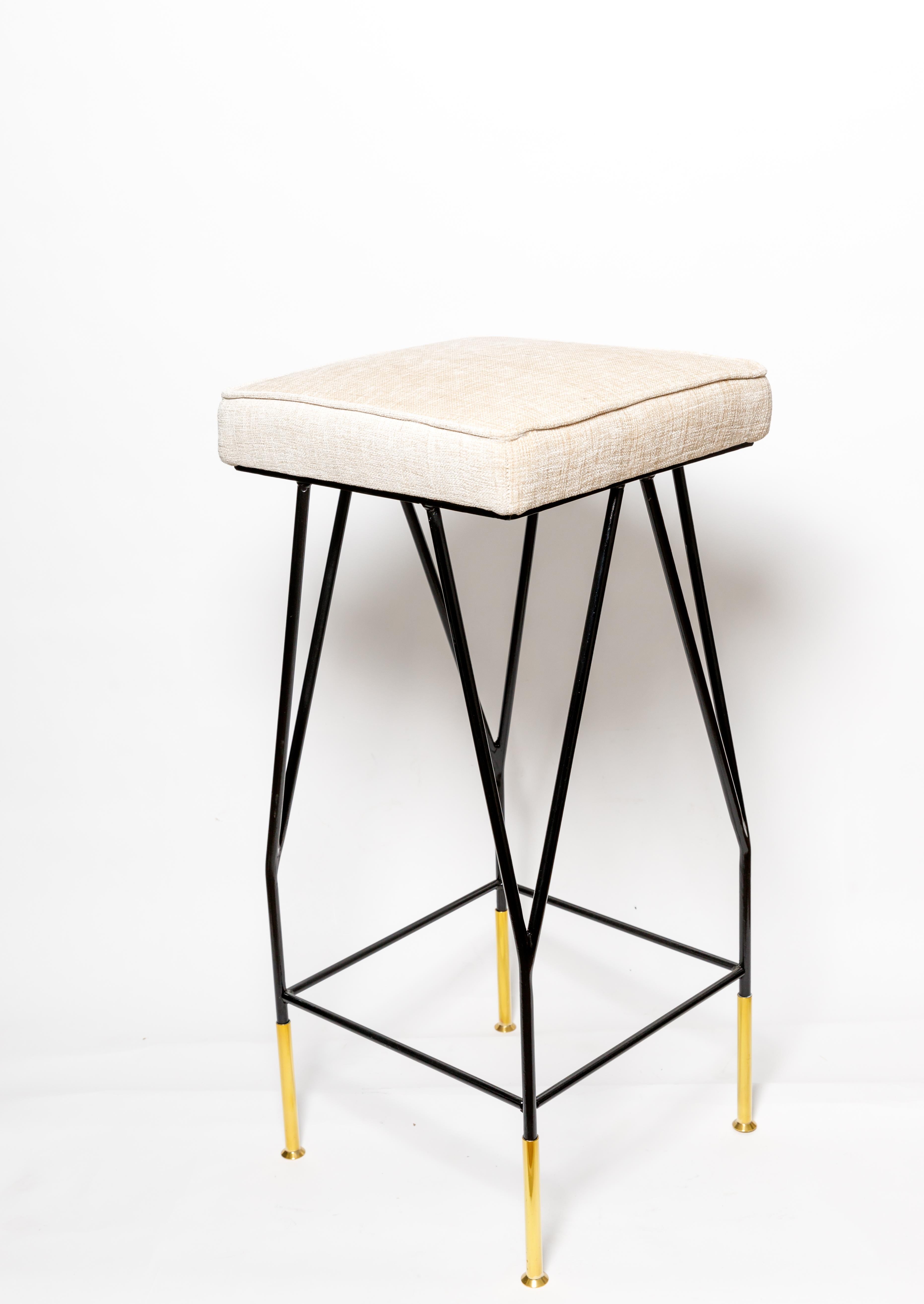 Upholstered enameled iron bar stools with brass details.
