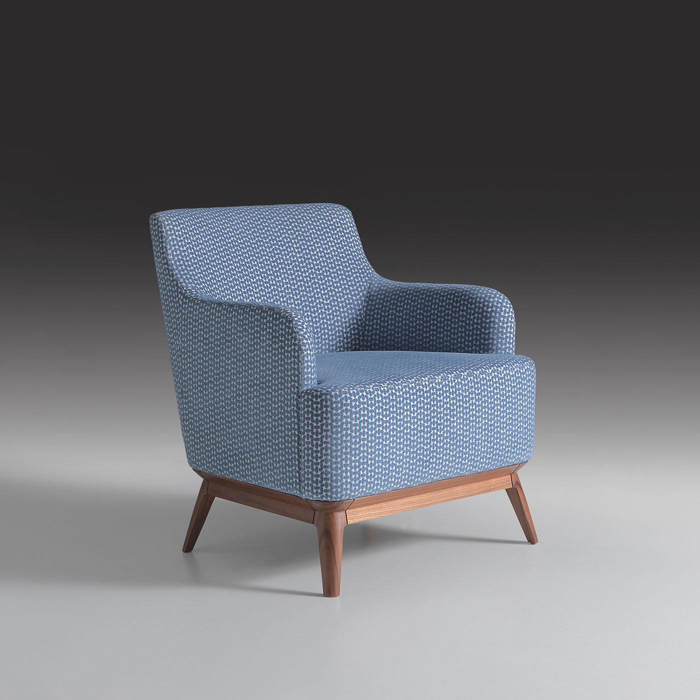 Distinguished by its wide seat and substantial padding, this upholstered armchair, with Canaletto walnut legs, stands out for its blend of comfort and versatility. Upholstered in Boogie fabric, it enhances a range of interiors, from stylish living
