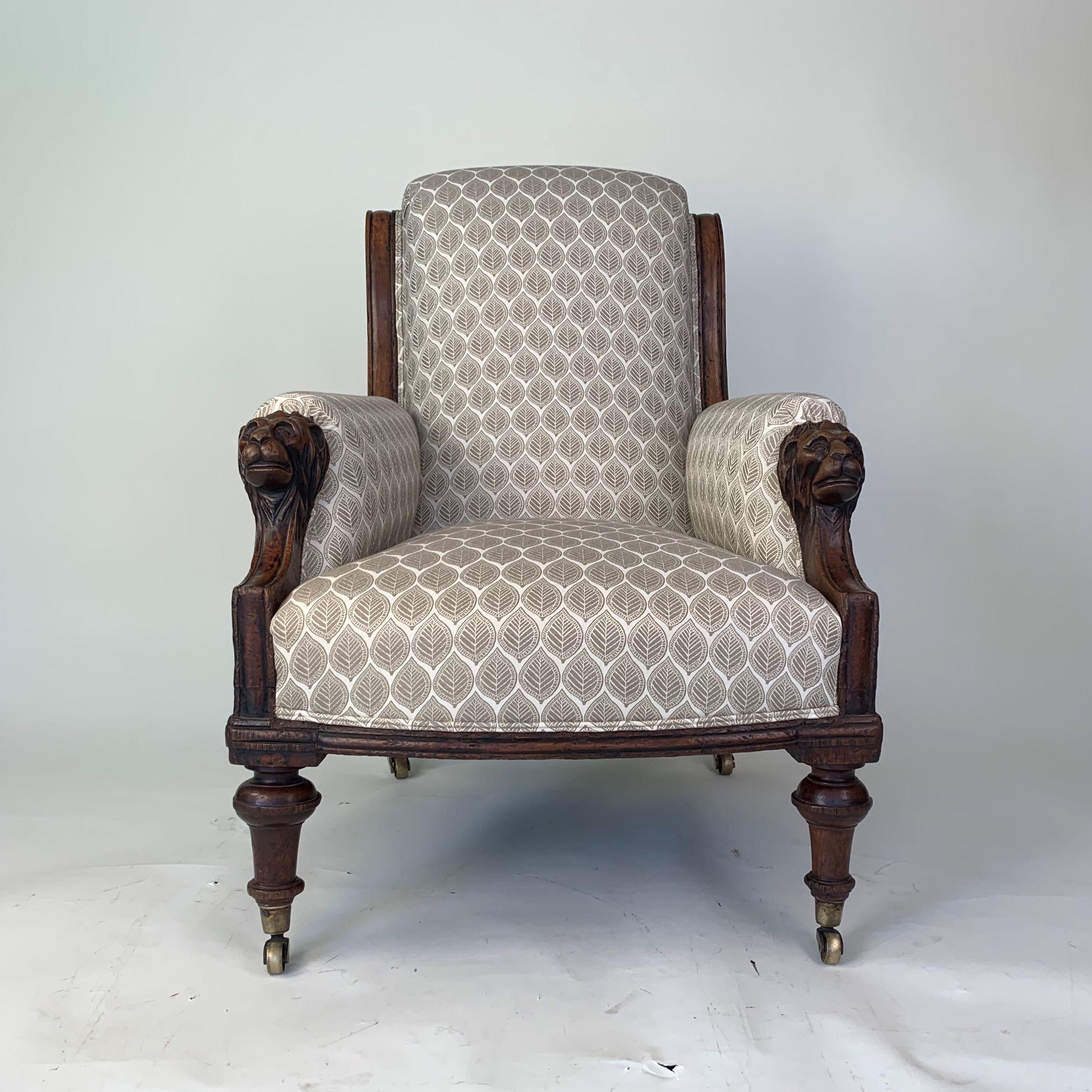An unusual mid 19th century stylish upholstered armchair with oak framed carved with lion's heads at the top of each arm. The swept back legs continuing upwards to form the sides of the backrest, and turned front legs of inverted vase form and