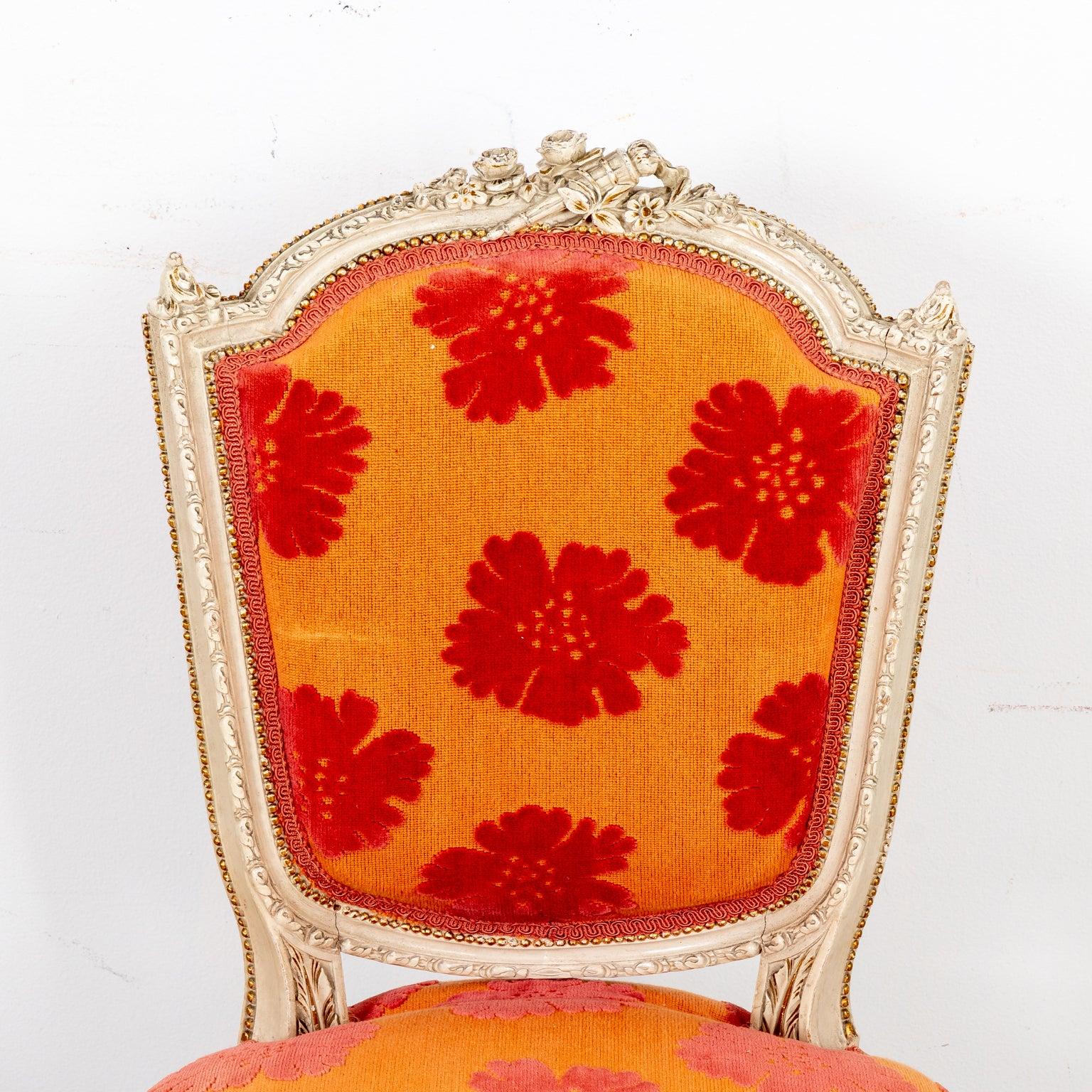 Red and orange floral upholstered Louis XVI style side chair with painted wood frame on round, fluted turned legs. The chair is detailed with a carved flower and flaming torch motif on the seat back, flower motifs on the front of the seat rail,