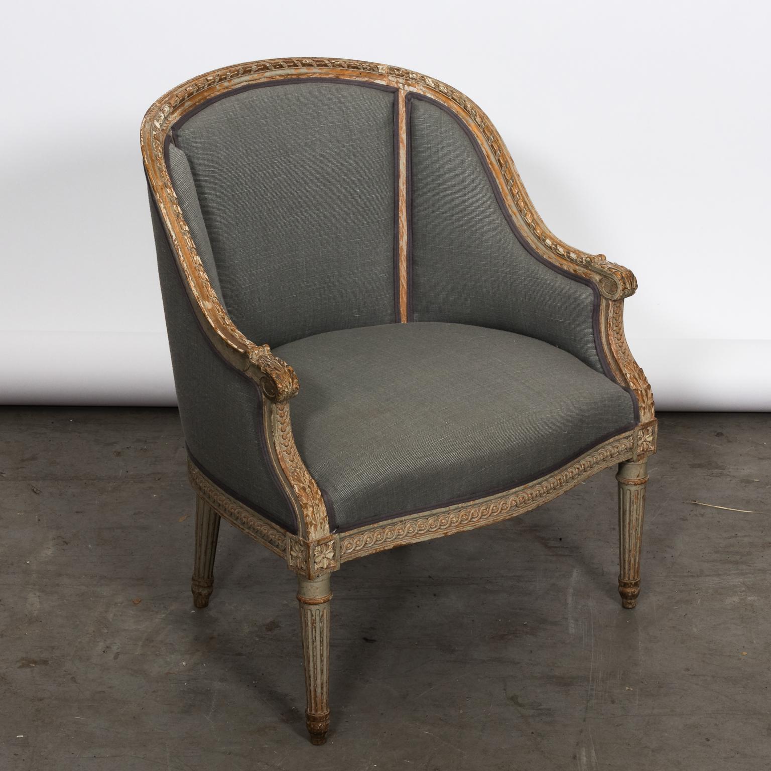 French Louis XVI style bergère style armchair with a curved back that features detailed carvings of rosettes, guilloche trim on the seat rail, and round fluted legs, circa early 20th century. Newly upholstered.