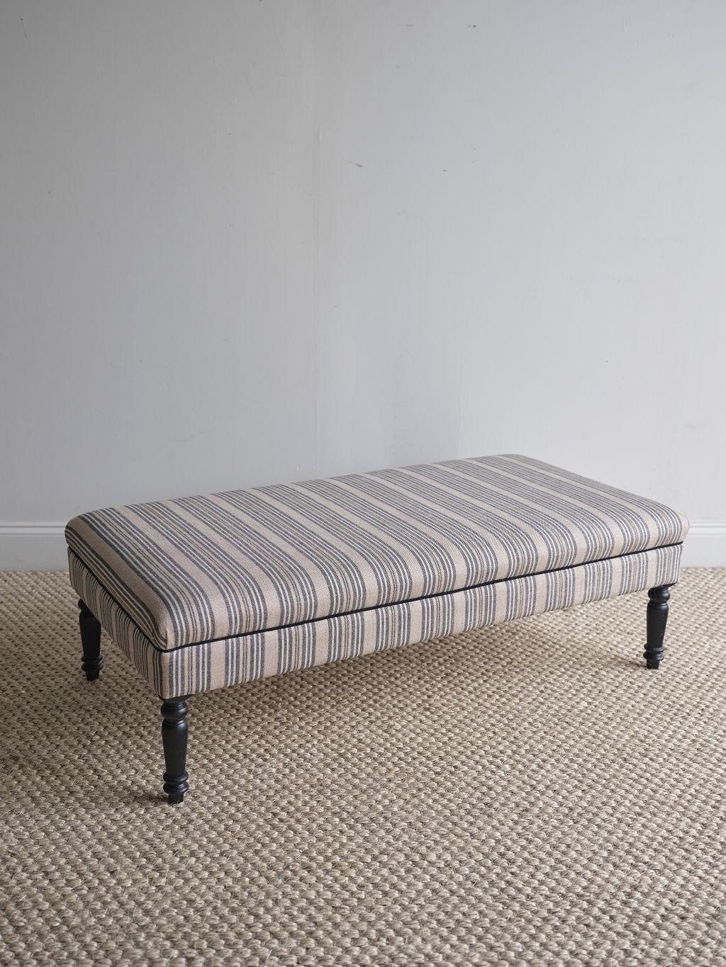 This lovely upholstered ottoman features black, white, and tan stripes and four black painted legs. It is in great shape and seems practically new, although it was built in the early 1900s. The fabric is in great condition and there are no rips or