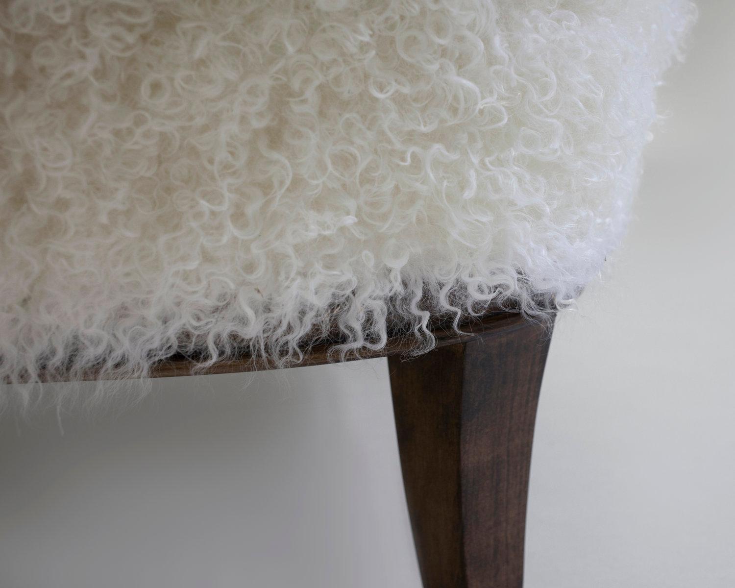 The Willow ottoman created to match the club chair of same name is shown in matching off white faux skin on wood stained legs. Hand carved and upholstered with feather and down seat cushion with metal leg caps. Made custom to your specifications as