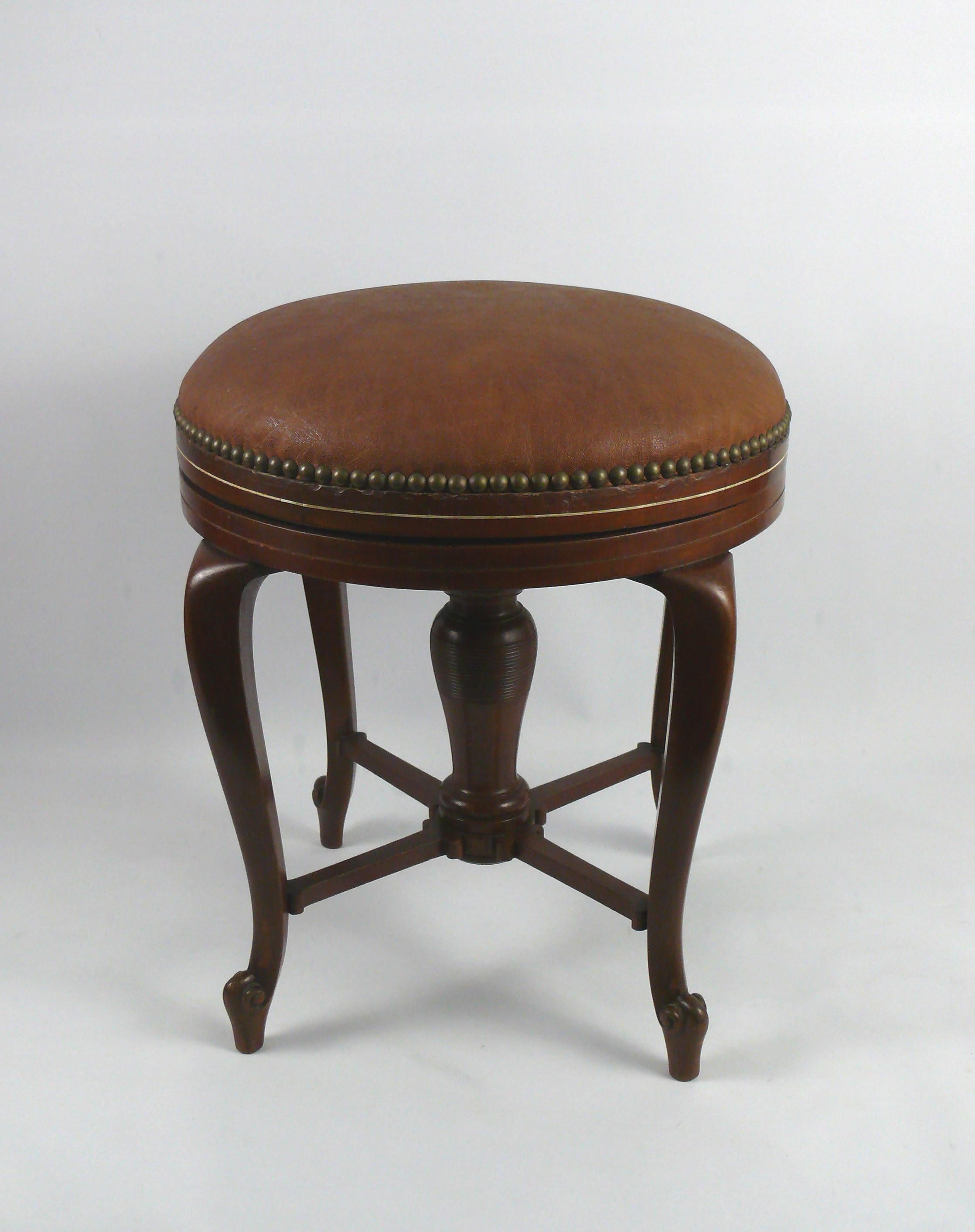 Elegant, very comfortable piano stool/swivel stool made of solid wood (walnut?) with padded leather seat. The piano stool has four curved feet that are glued into a ring at the top and glued to the turned center column with a wooden cross at the