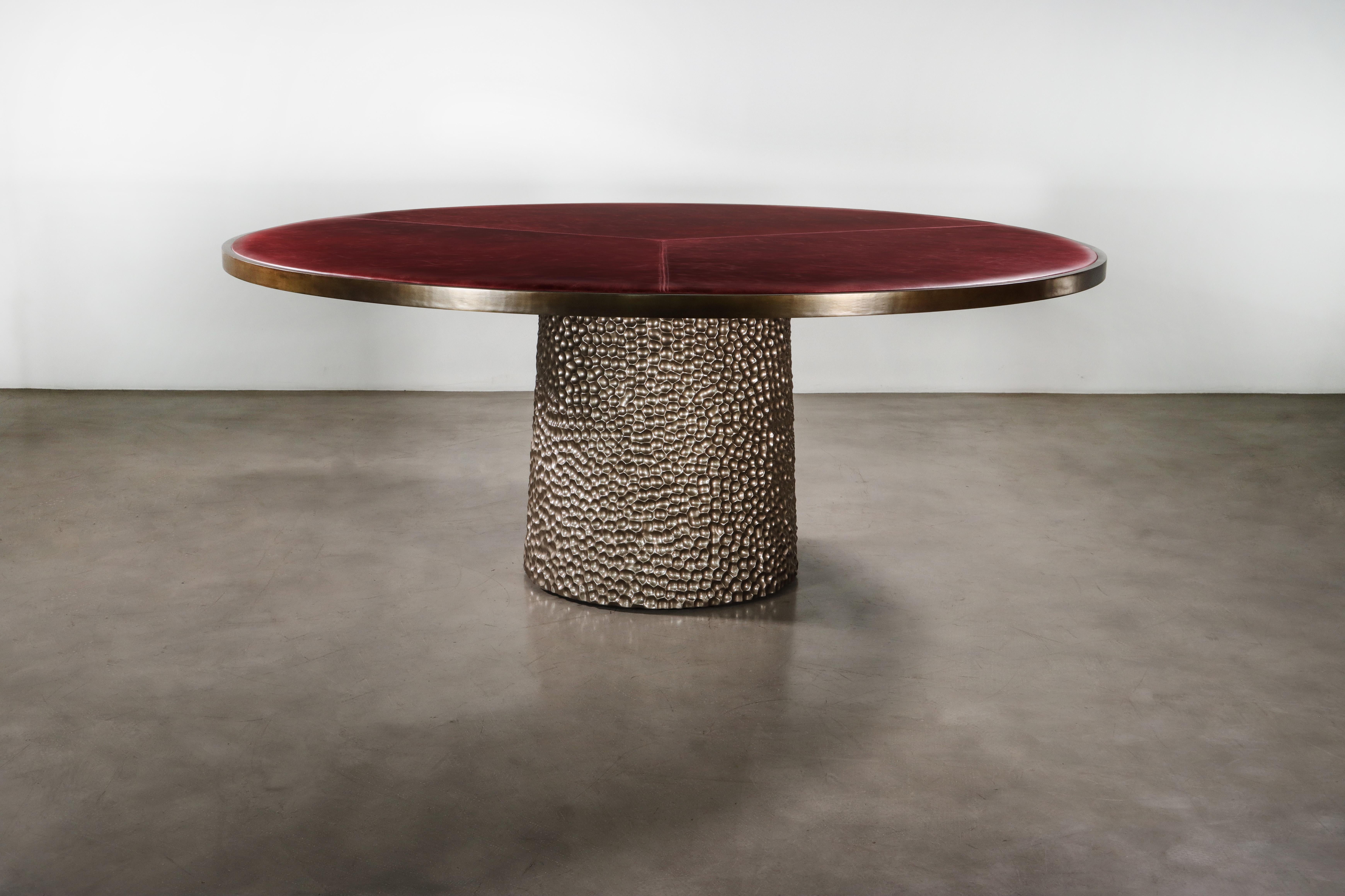 Der Giada Tisch verfügt über eine gepolsterte Platte aus Stoff oder Leder Ihrer Wahl mit einer eleganten Bronzeverzierung und einem handgeschnitzten Holzsockel, hier in einer Metallic-Ausführung.  

Die Maße sind 72