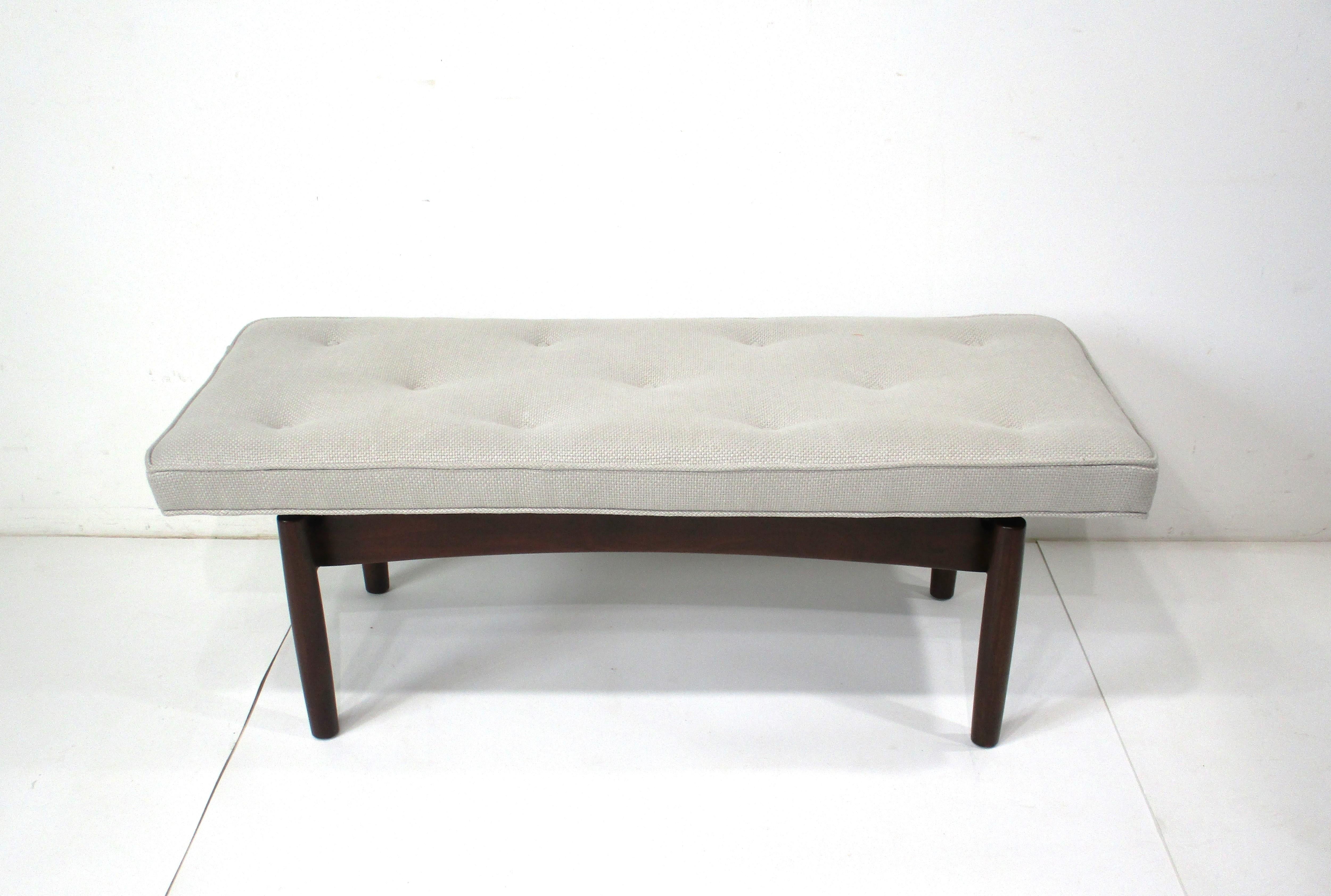A mid-century bench with upholstered button top cushion in a soft gray Cream woven contract fabric. The bottom frame is in a dark walnut with very sturdy legs and a small cut out to the ends giving the cushion a floating affect. Designed in the