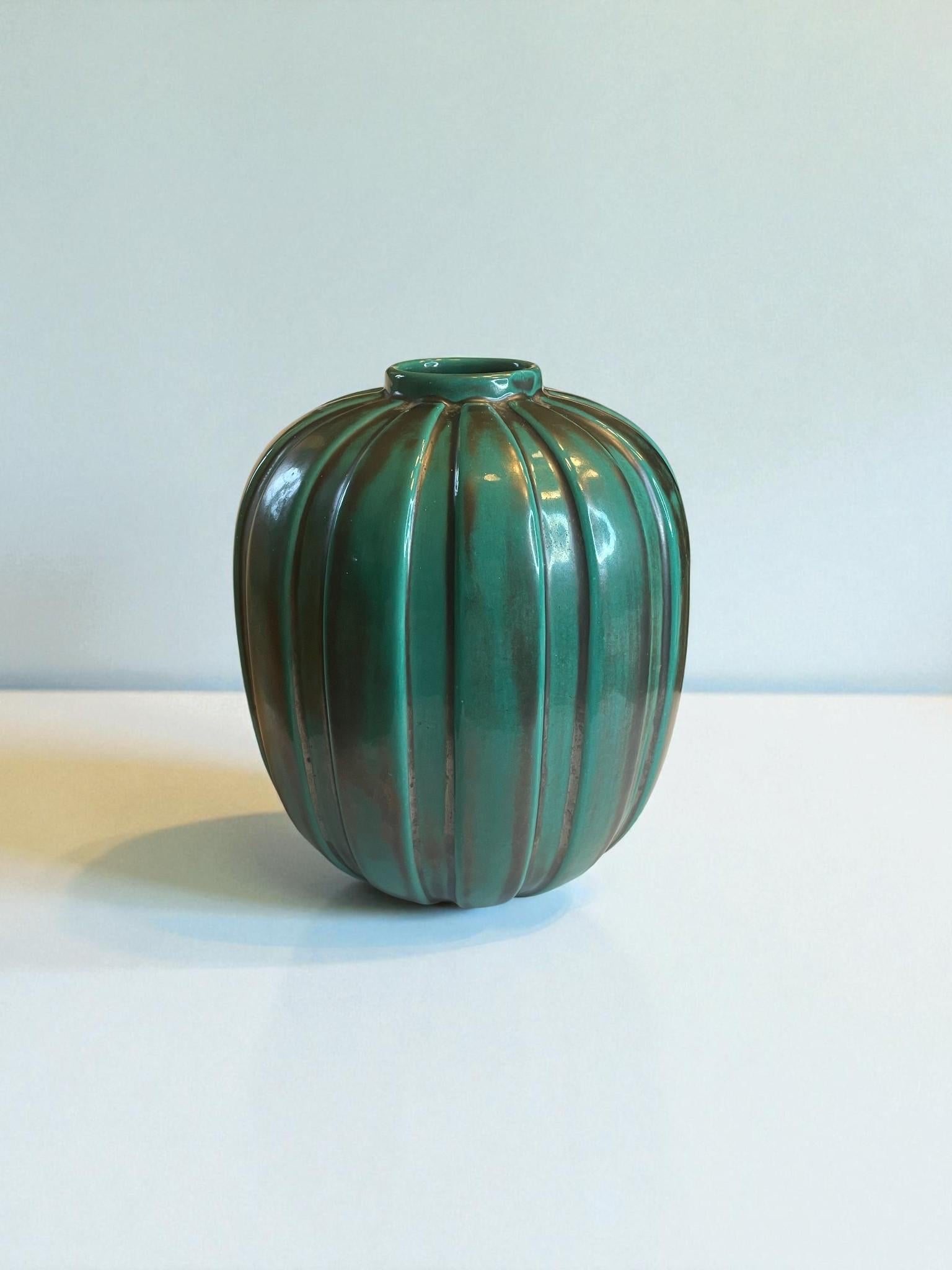 Un elegante vaso scultoreo di Upsala Ekeby, Svezia, risalente agli anni '30.
Il pezzo è caratterizzato da una forma arrotondata a coste con un ricco smalto verde intenso che passa sottilmente attraverso toni più scuri e più chiari, creando
