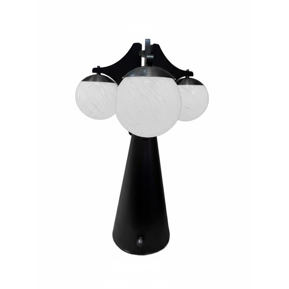 una lámpara de sobremesa que exhibe una silueta escultural con dos pantallas cónicas de tejido semitranslúcido, diseñadas para difundir la luz con un suave resplandor ambiental. su esbelto pie y base están fabricados en latón anodizado patinado en