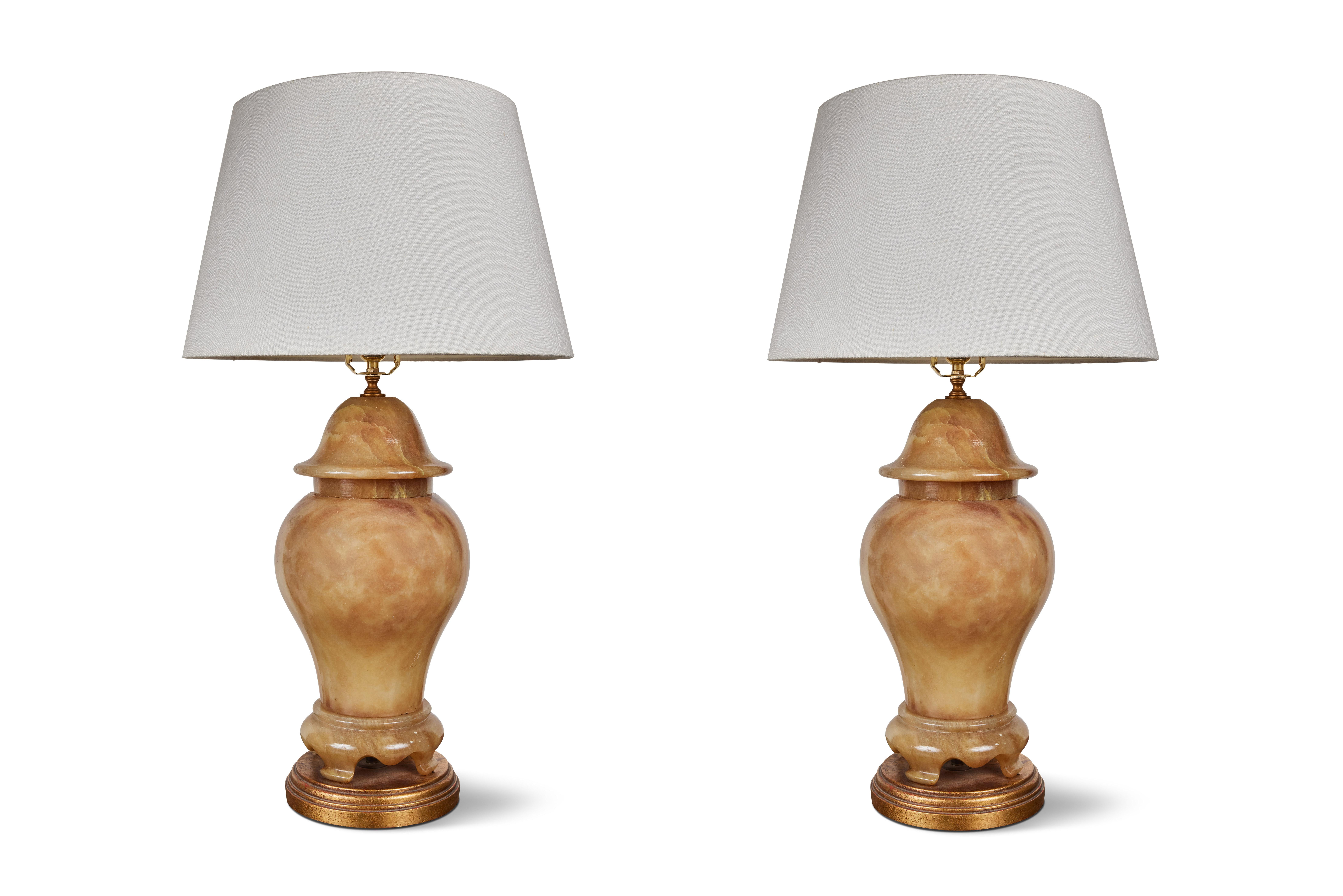 A pair of elegant, carved and polished, alabaster table lamps in the Chinoiserie taste. Each with a faux lid and a serpentine feet above a stepped, giltwood base. These dynamic lamps can be lit in three ways, including from within, as can be seen in