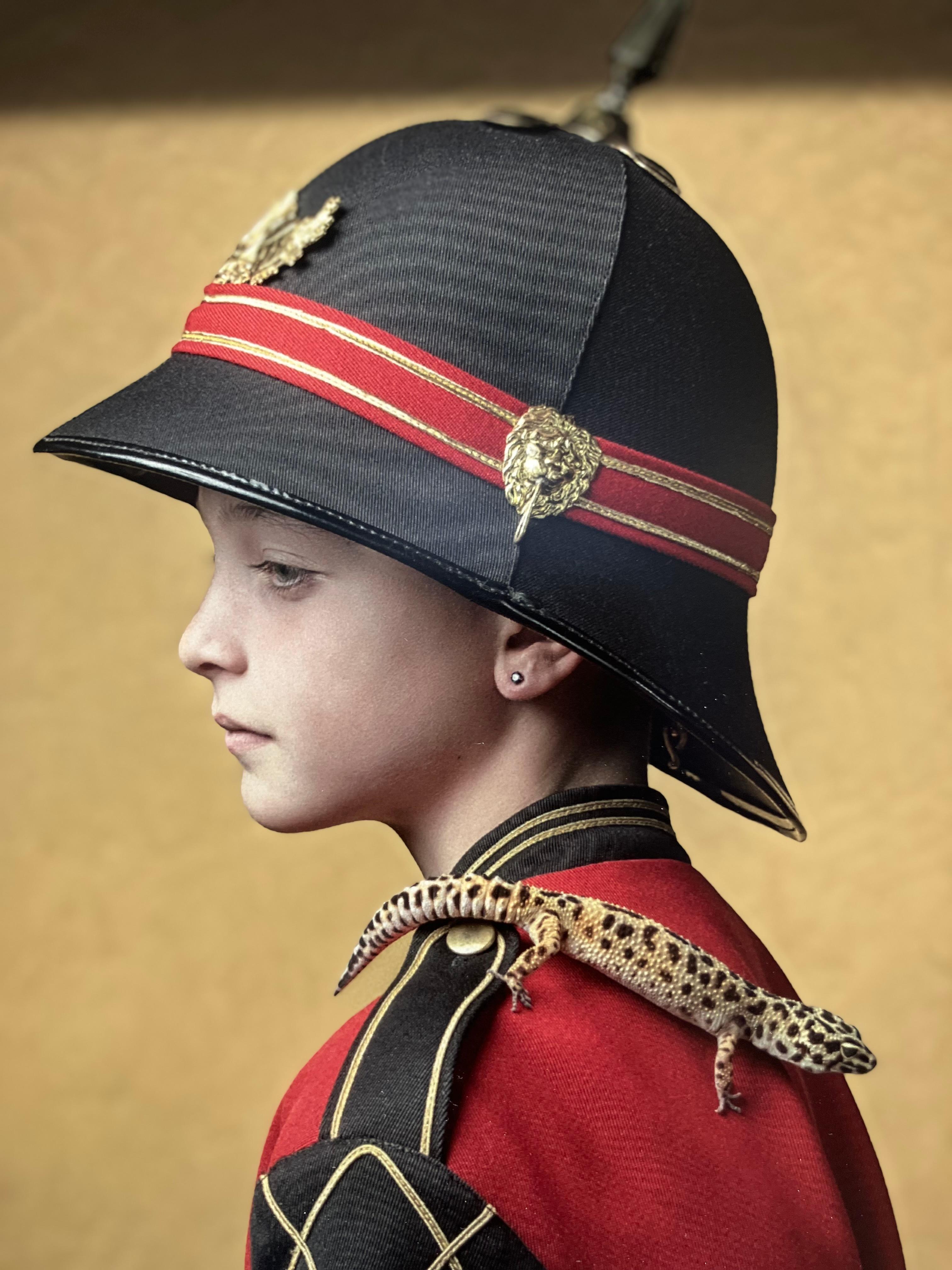 ''Lukah 2'' Dutch Contemporary Portrait of a Boy in Red Uniform with Gecko - Brown Figurative Photograph by Ursula van de Bunte