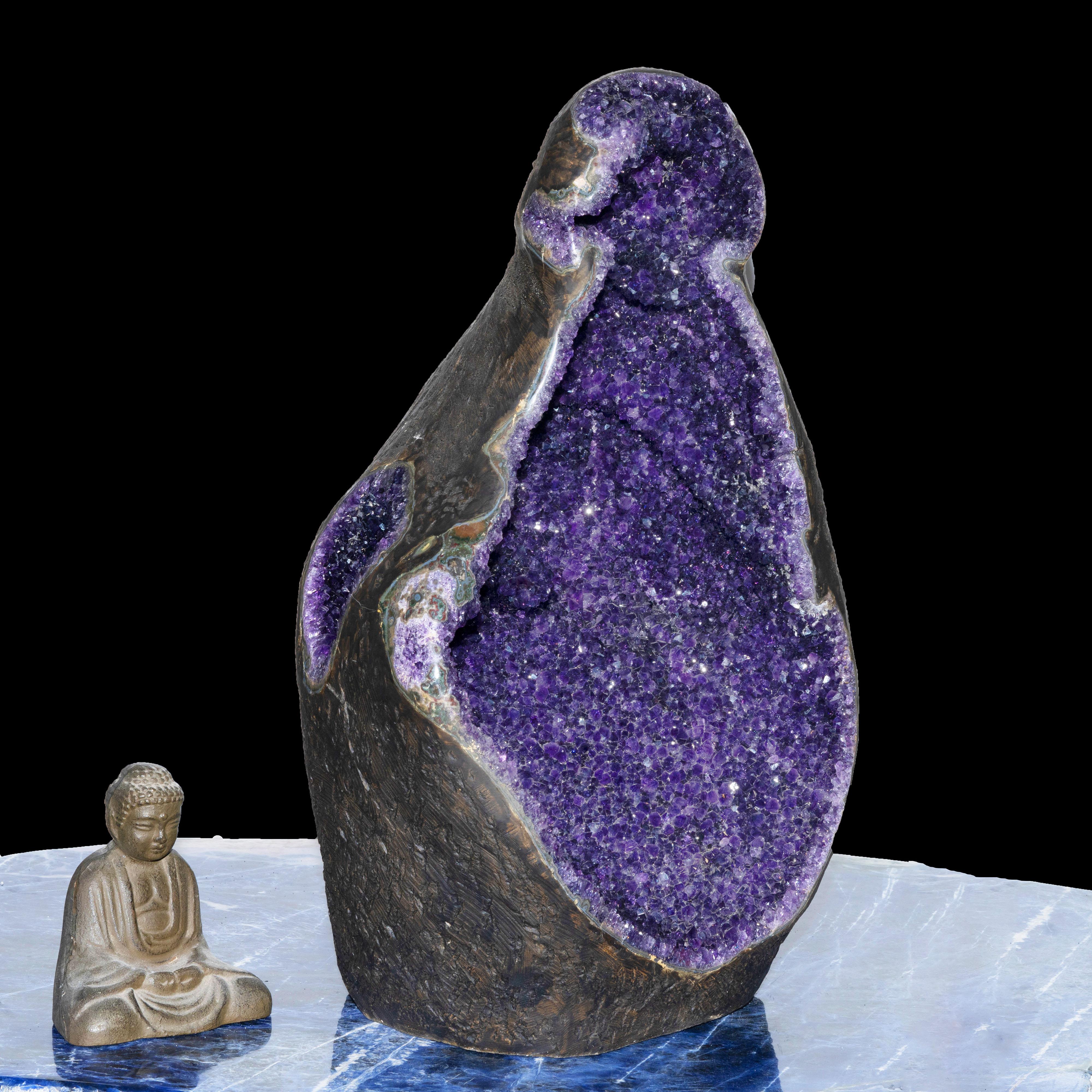 This over one and a half foot tall more than fifty pound sculptural amethyst geode from Uruguay glistens from within with a lustrous coating of naturally terminated, fully formed deep purple amethyst crystals. Featuring a stalactite and natural
