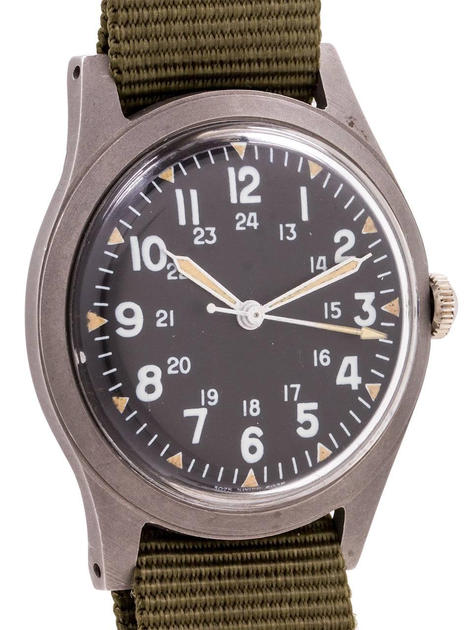 
US Military issue Benrus man’s wristwatch post Vietnam era featuring 34 X 41mm non reflective brushed finish base metal case, acrylic crystal, and original matte black dial with 24 hour indexes and triangular luminous hour indexes, luminous hands
