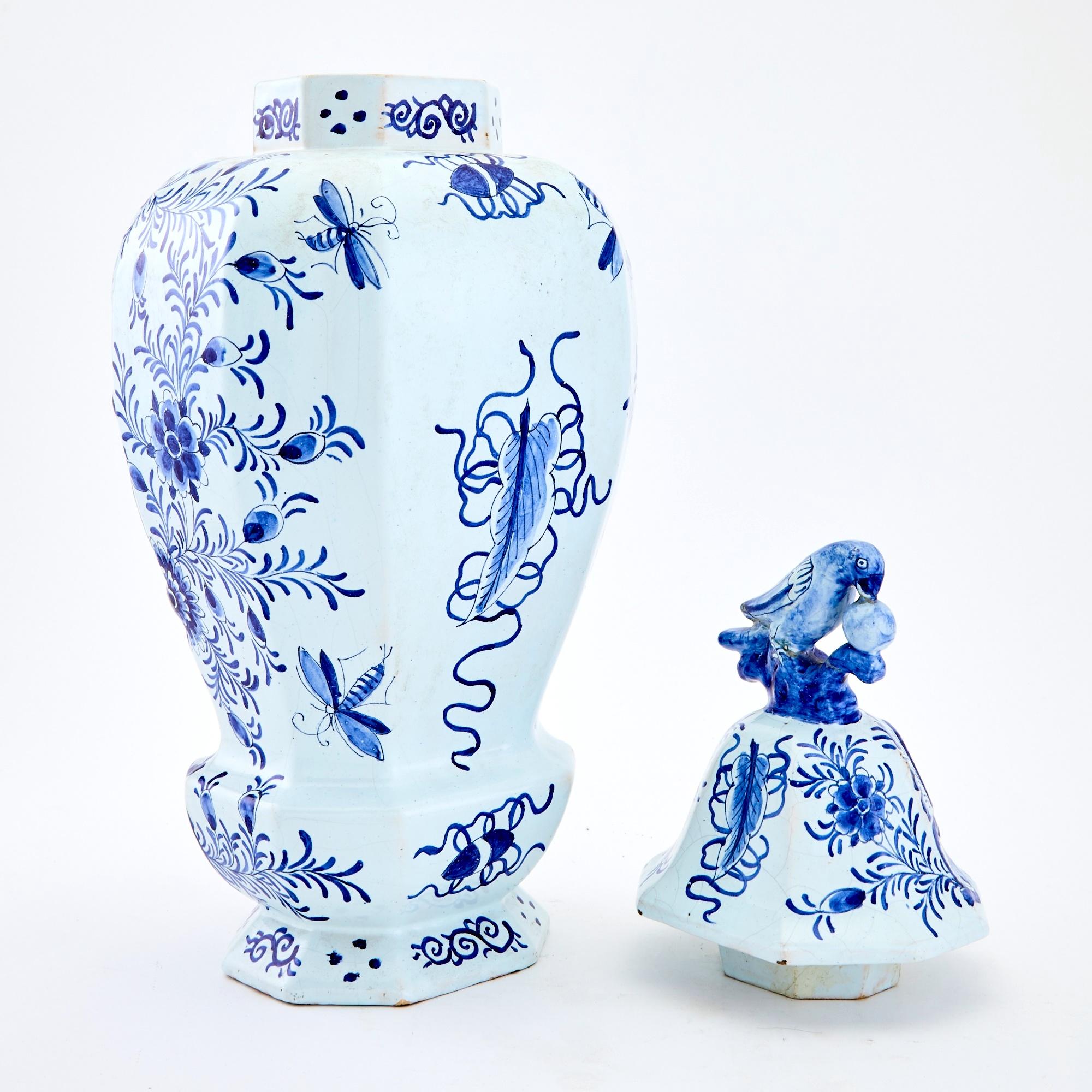 Tauchen Sie ein in die bezaubernde Welt des frühen 19. Jahrhunderts mit dieser exquisiten, blau-weiß glasierten Keramikurne aus Delft. Dieses dekorative Stück mit zeitlosem Charme besticht durch die Vogelskulptur, die seine mit einer Krone bedeckte