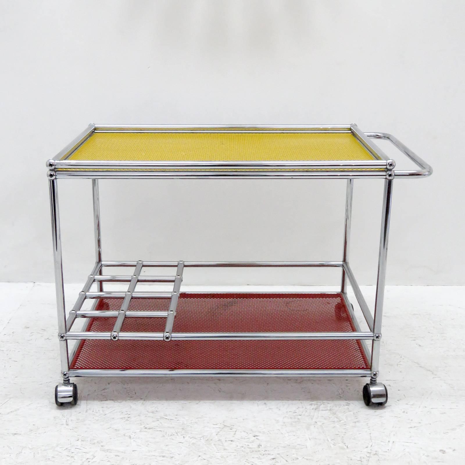 Stunning bar cart by Fritz Haller & Paul Scharer for USM Haller, two-tier modular chrome frame on casters with unique red and yellow powder-coated perforated metal shelves, frame includes eight bottle compartments, can be extended with additional
