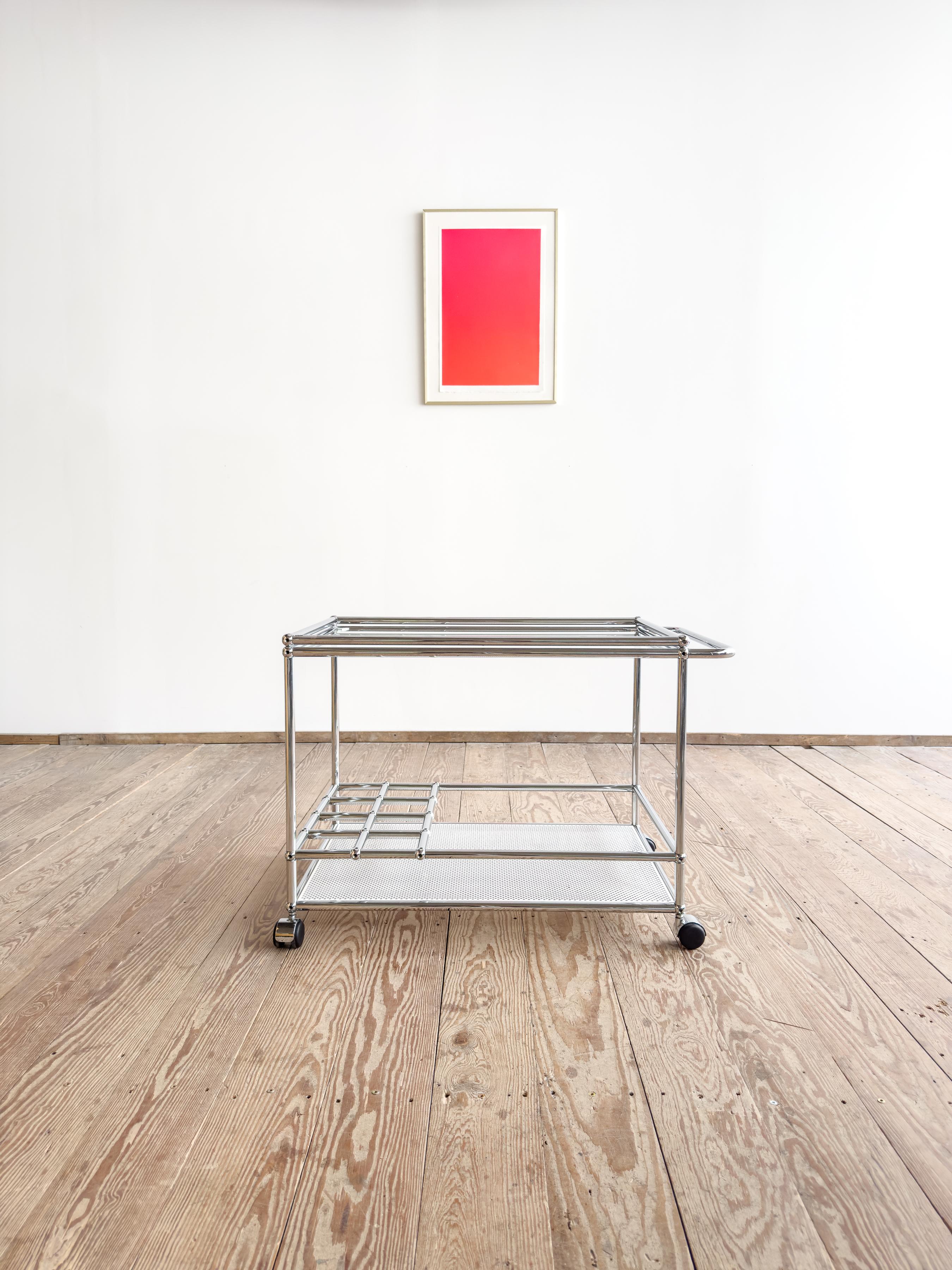 Elegant and multifunctional USM Haller bar cart / tea trolley / serving trolley, made in Switzerland and known for its modular elegance and timeless utility.

The piece features a white perforated metal shelf on the bottom, with an intermediate