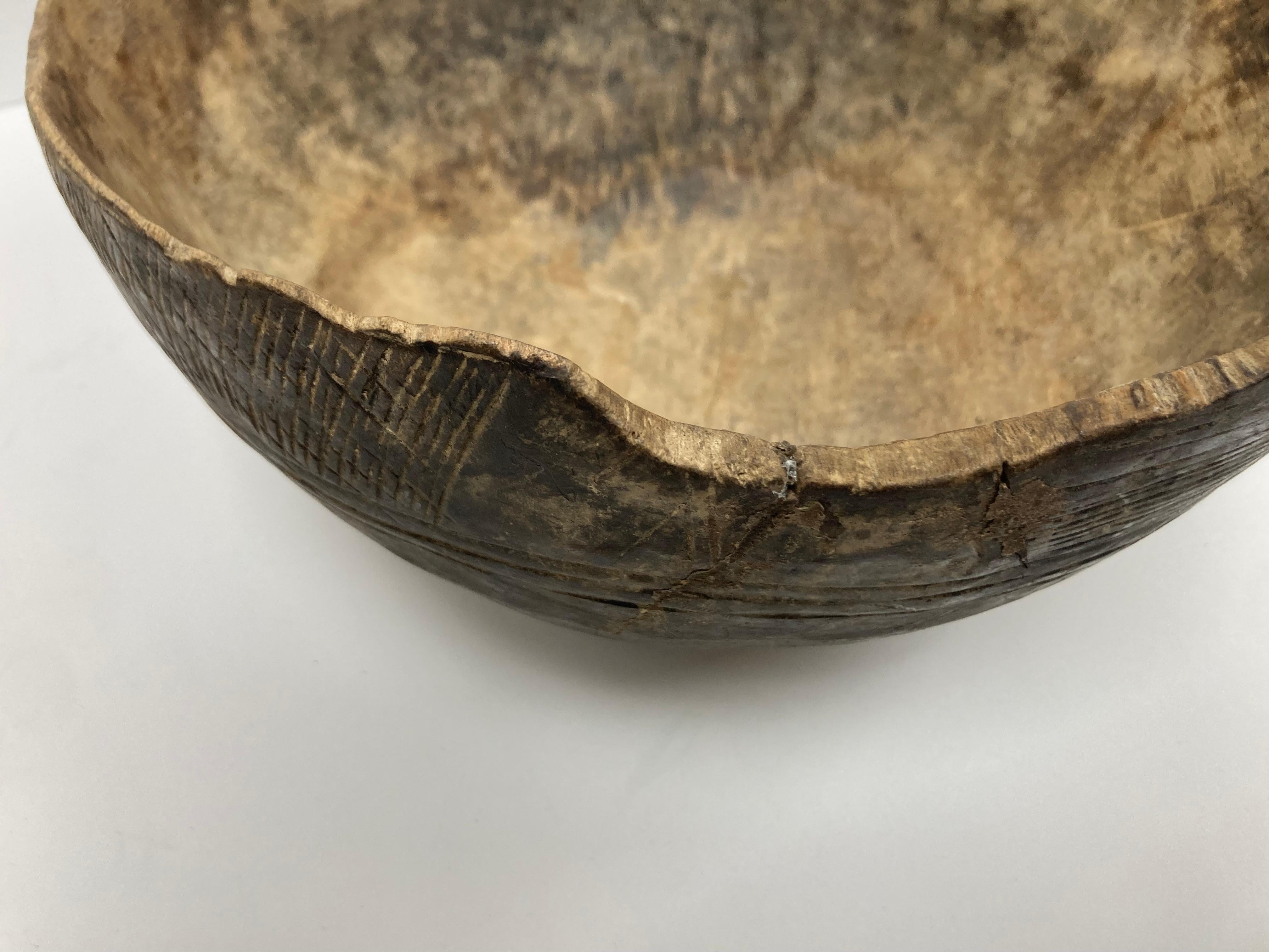 Una grande e ben usurata ciotola in Wood africano con una bella presentazione naturale. La ciotola presenta un'ampia fascia di motivi geometrici incisi sul bordo esterno e due fori sul bordo per l'utilizzo di una cinghia di cuoio (ora mancante) per