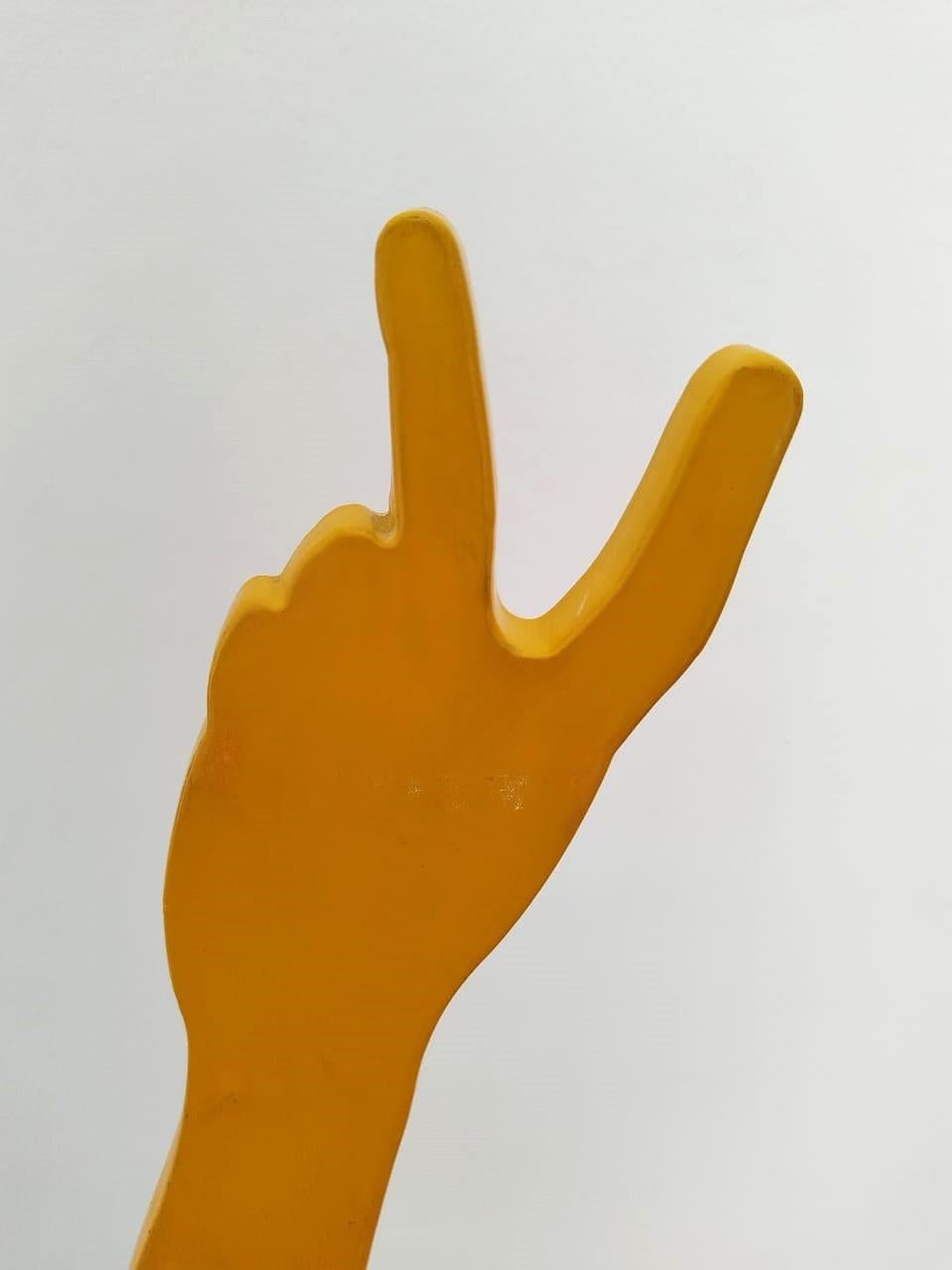 Eine Skulptur aus gelb pulverbeschichtetem Baustahl in limitierter Auflage auf einem schwarzen Stahlsockel. Die Skulptur ist typisch für Uwe Pfaffs augenzwinkernde Herangehensweise und stellt einen menschlichen Arm dar, der ein Friedenszeichen