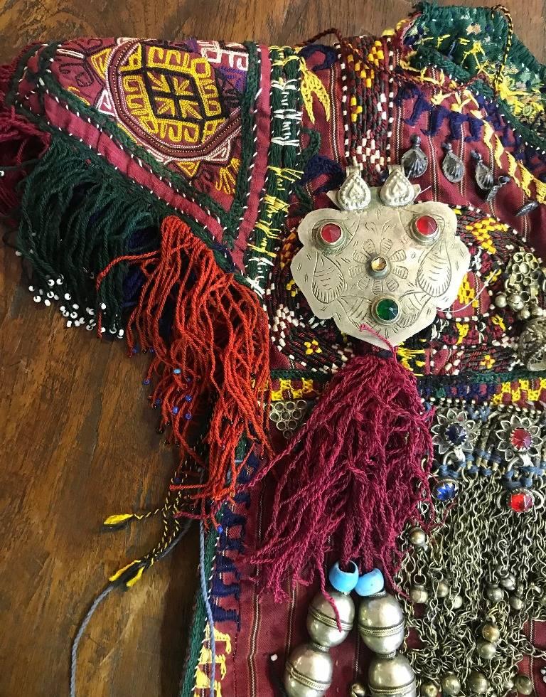 The vintage ethnic dress is heavily adorned and decorated (both front and back) by hand with colorful tassels, metals, trinkets, silver (We believe the dress is made of some silver pieces though we can't confirm as we haven't personally tested),