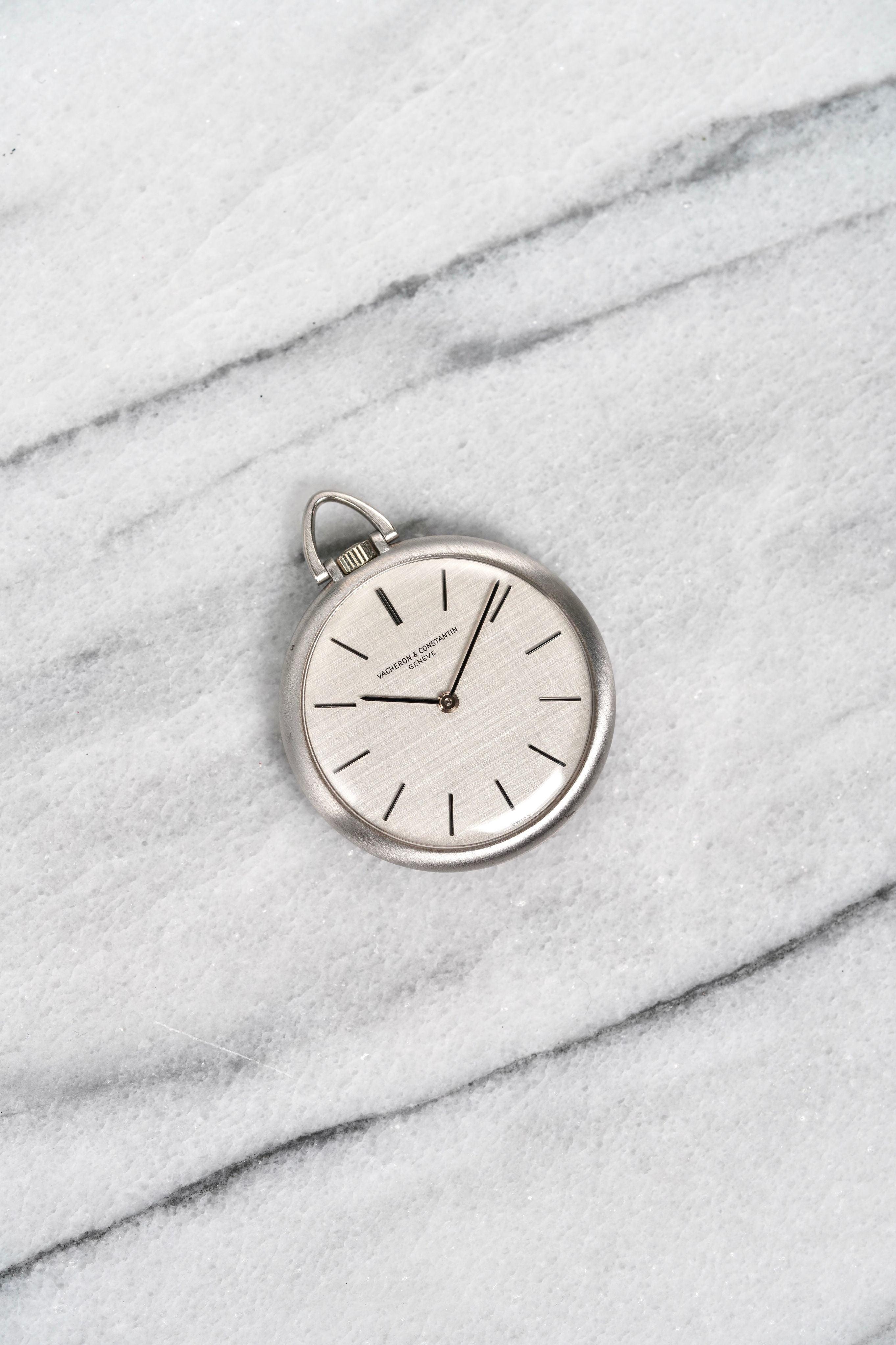 Aquí tienes un reloj de bolsillo Vacheron Constantin de cuerda manual de oro blanco de 18 quilates con esfera de lino plateado de la década de 1970. Las medidas incluyen una caja de 33 mm. Agujas de bastón y marcadores de hora a juego. 26,4 gramos.