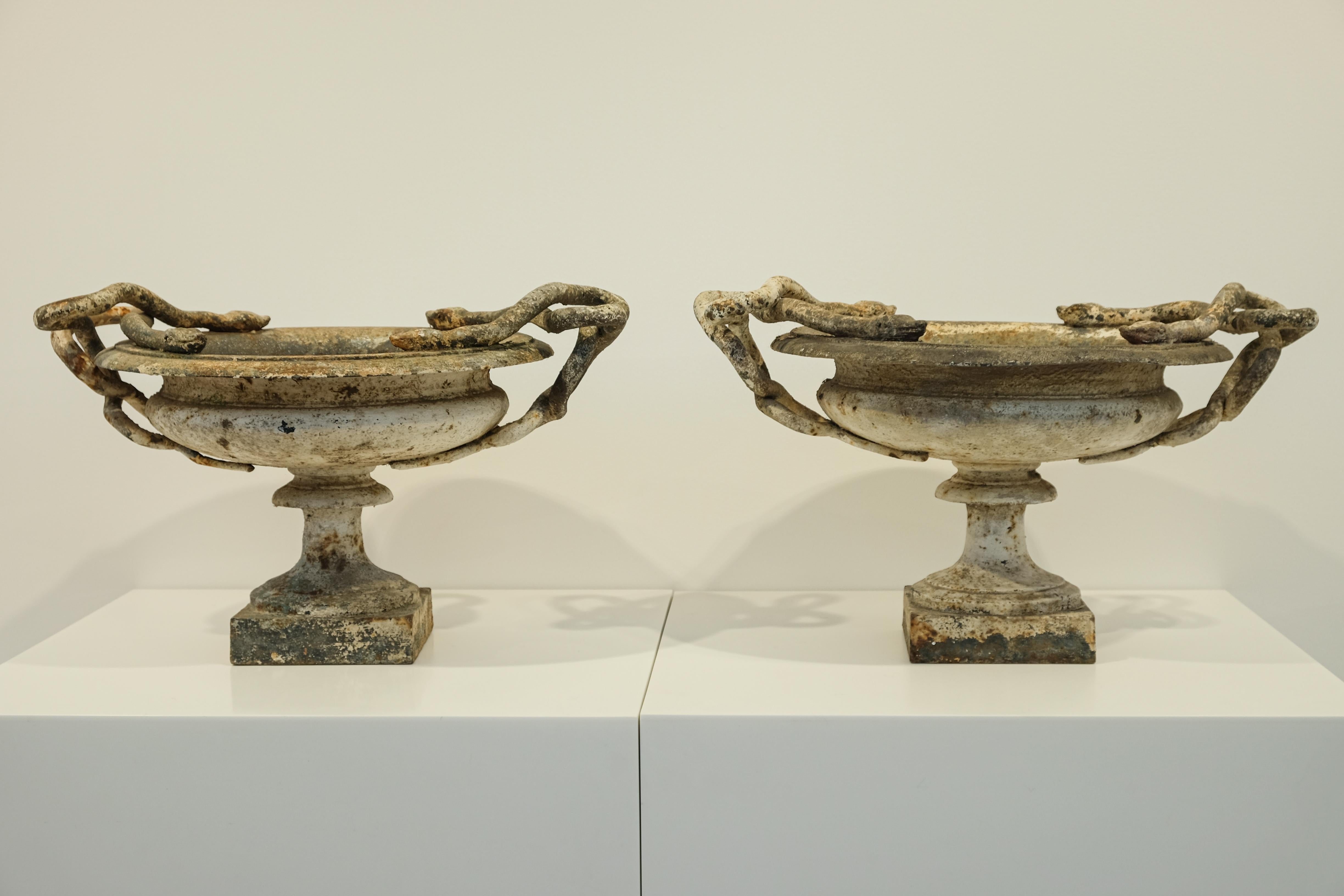 A small pair of white cast-iron urns with intertwined snakes. Marked with a “1” to denote the smallest of three sizes made by the renowned Val d’Osne Foundry. The smallest size is particularly rare. Exquisite tones of white, brown, and rust with a