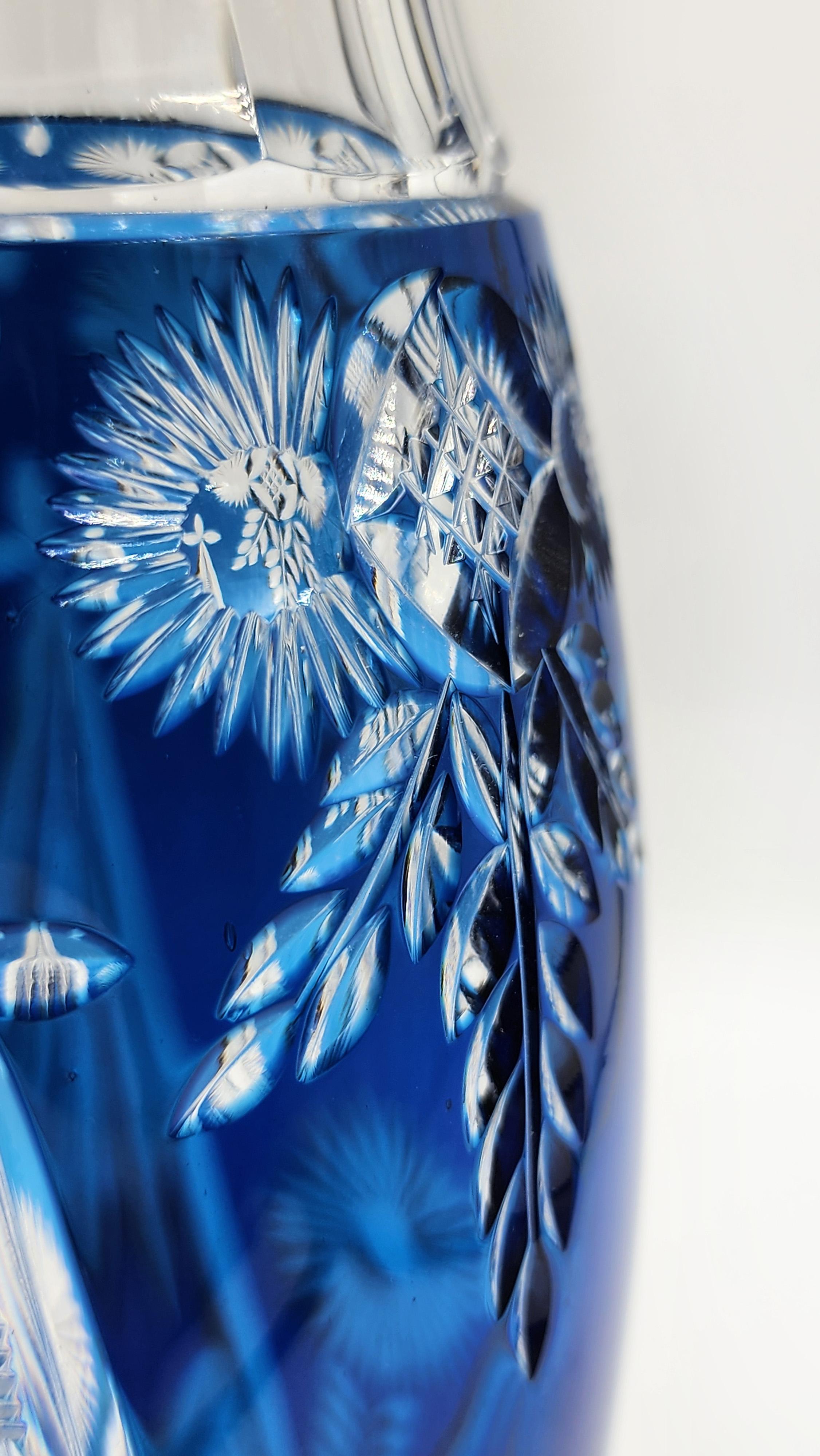 Val Saint Lambert Cut Glass Vase
The Val Saint Lambert cut glass vase features a design with intricate floral and geometric motifs carved deeply into a cobalt blue glass body. The carving reveals the underlying clear glass, creating a striking