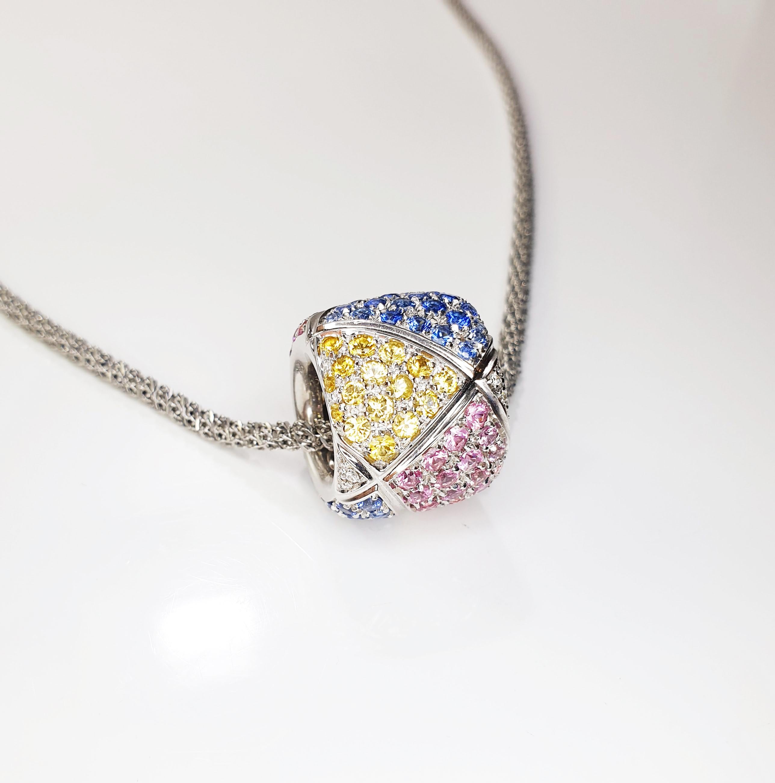 Collezione Clash Una danza arcobaleno di zaffiri multicolori blu, rosa e gialli 93 pezzi di 0,02ct per un totale di 18,6ct di zaffiri e 3,45ct di diamanti. 
Il  Il ciondolo in oro bianco 18k pesa 15,9 grammi 
Le opzioni di catene sono su richiesta. 