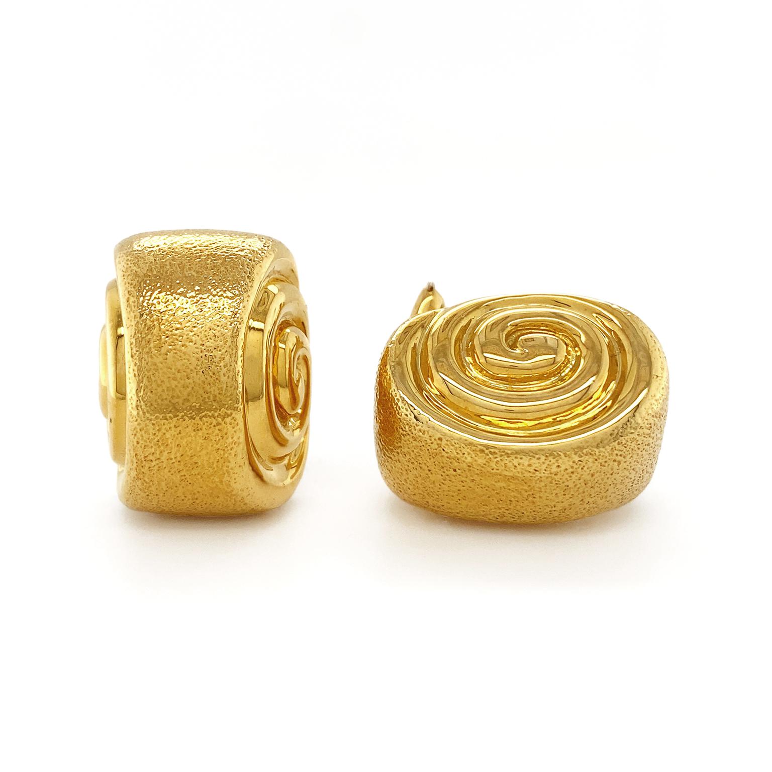 Light reflects in many ways from these earrings. The body is made of 18k yellow gold curled tight. Down the center are many tiny indents, creating a softer sheen. On either side is a tight spiral of smooth gold. Light forms sharp lines, some aimed
