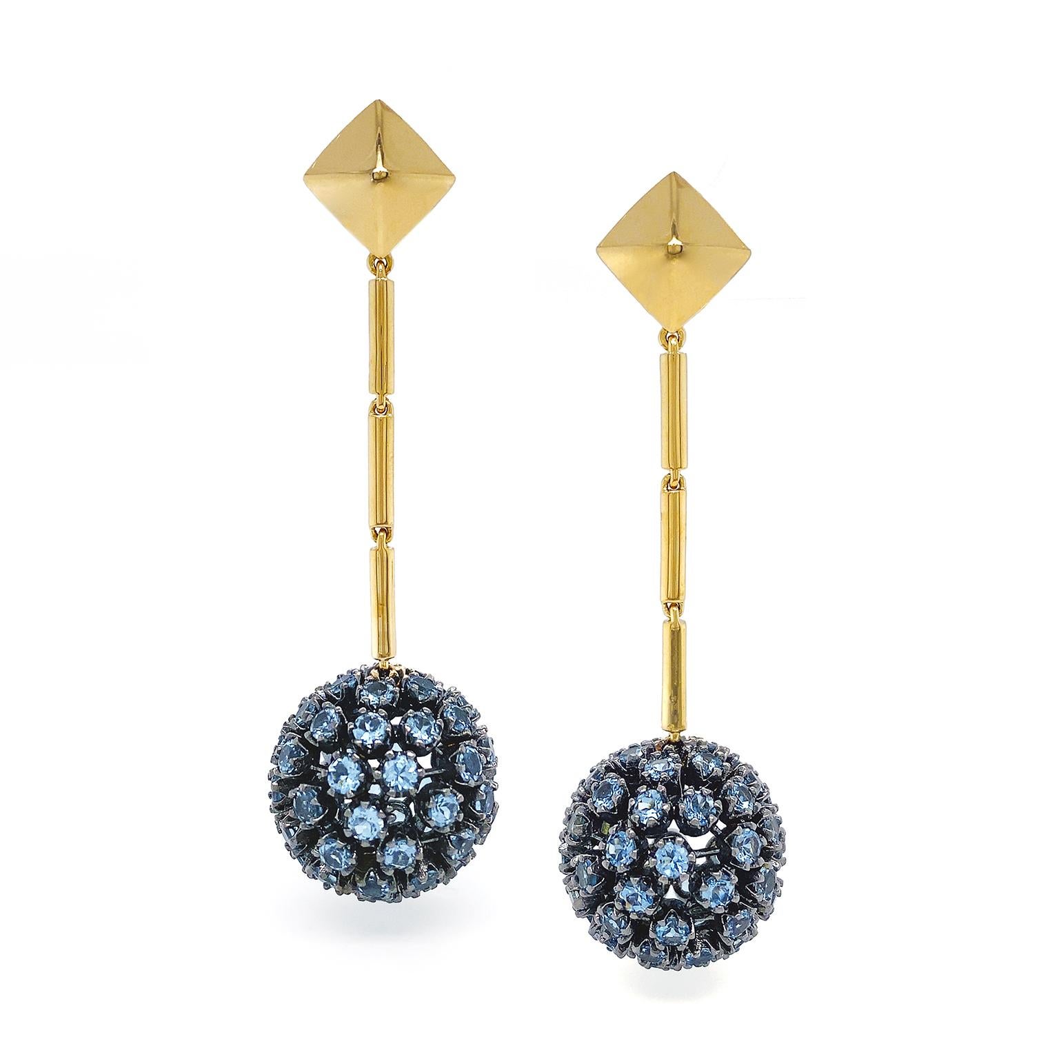 Coruscating light of aquamarine is showcased in these elegant drop earrings. The design begins with an 18k yellow gold pyramid, which connects to a row of three slender bars. Next, against the black rhodium setting, a globe suspends embellished with