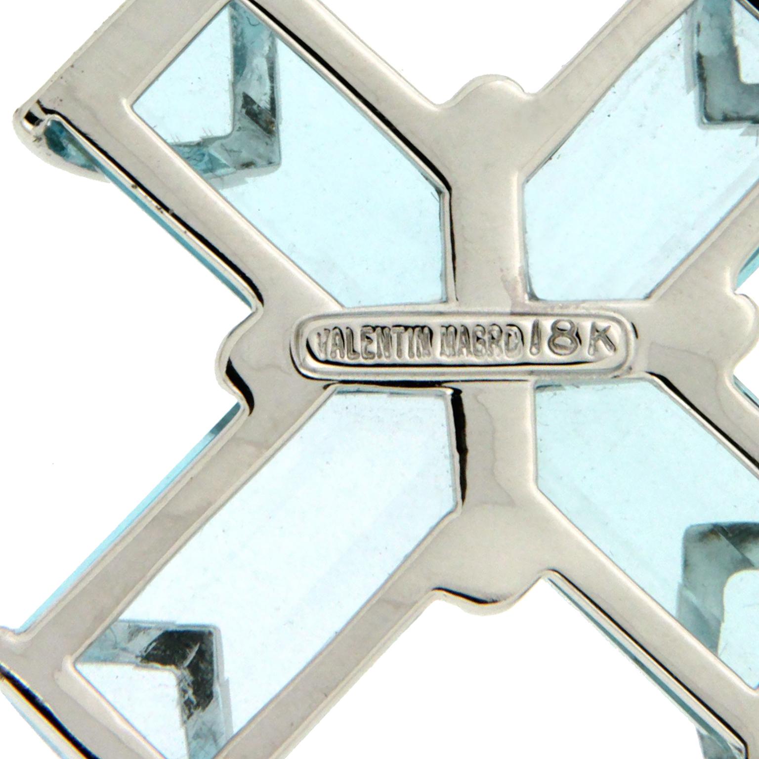 White gold accompanies the light-hued blue topaz for this pendant. Four-step cuts of the gem create the shape of a cross. 18k white gold overlaps from opposite directions in the center, forming an X. Each end of the cross also has V-shaped