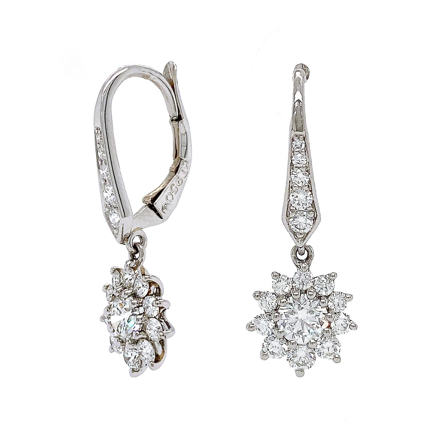 These drop earrings portray diamonds as stars. VS1-VVS2 clarity round brilliant cut diamonds are coupled with 18k white gold for these earrings. Diamonds in the hooks lead toward the drop of smaller ones that frame a larger diamond in the center in