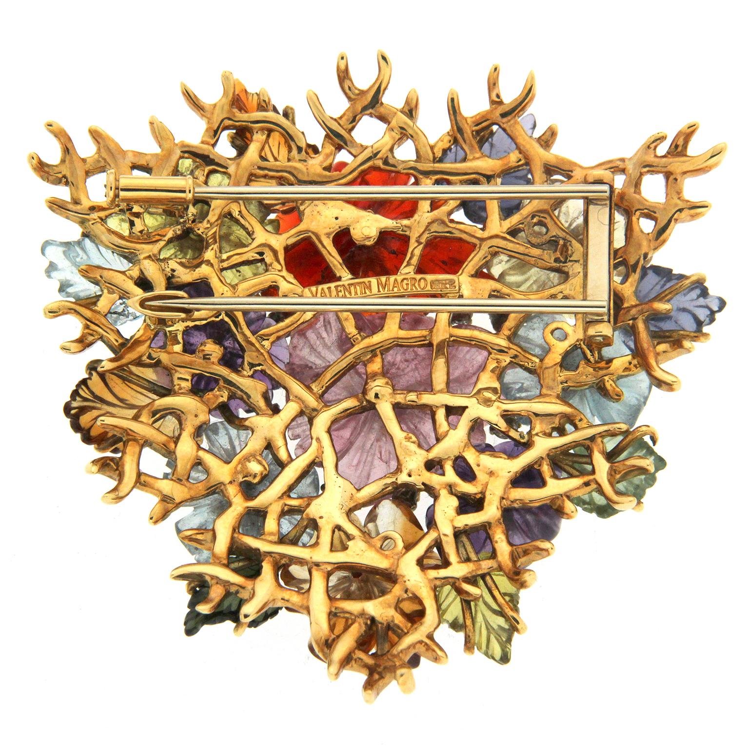 Flowers illustrated in jewels erupt from this brooch. Hand-carved colored gemstones are textured with scalloped edges to form flowers in various sizes. Brilliant cut diamonds bring light to the centers of each. Gemstones also form tapered leaves,