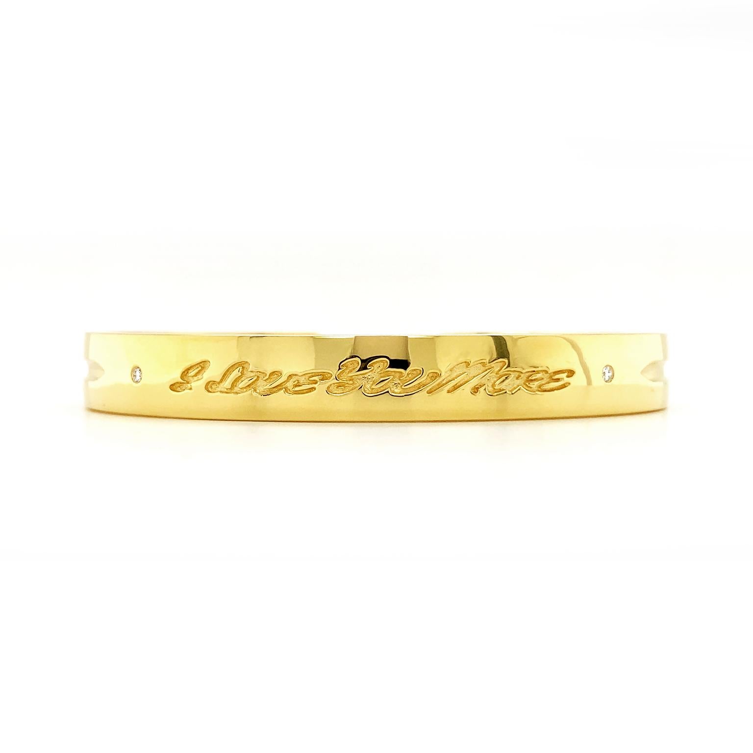 This bracelet is engraved with love. The 18k yellow gold bangle is polished smooth, with grooves and hinges for the wearer’s convenience. The words 'I love you more' are written in cursive upon the surface. Round brilliant cut diamonds flank the