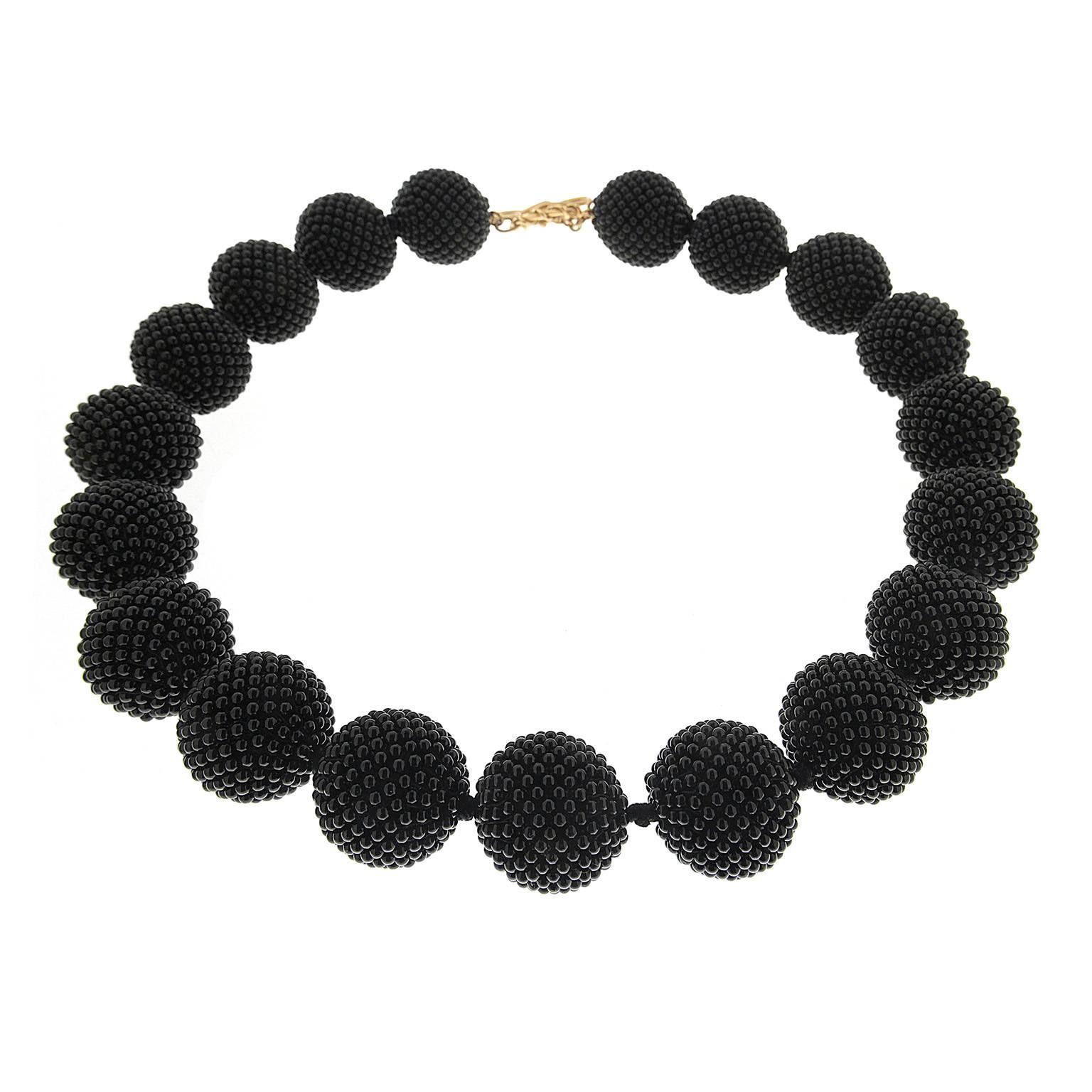 Valentin Magro Large Onyx Woven Ball Necklace feature complex beads. Tiny onyx pieces are woven into 19 balls, creating a textured surface. They’re placed on a single strand, with a knot between each ball. An 18k yellow gold knot and toggle clasp