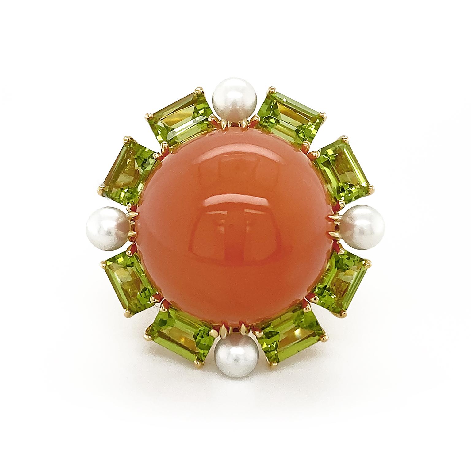 As the crown, orange moonstone is carved into a polished round cabochon which emits a glossed light. Encasing the gem are emerald cut peridots, with a pearl in between each pair of emeralds for a luminous contrast. 18k yellow gold forms the band