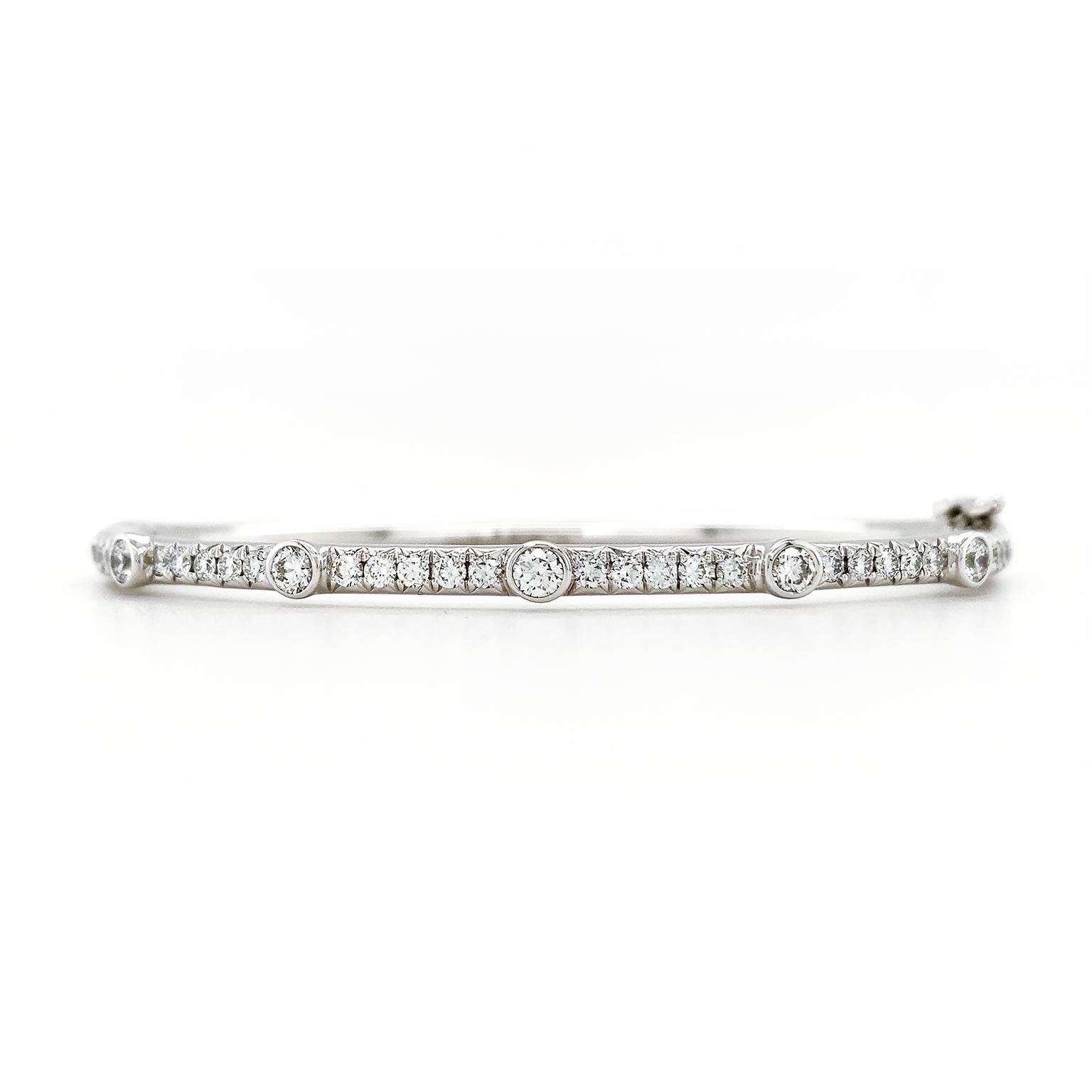 An 18k white gold bangle is enhanced by the glimmer of pave set diamonds. 5 bezel set round brilliant cut diamonds are carefully spaced throughout the bracelet for added radiance. A hidden clasp secures the bracelet. The total weight of the diamonds