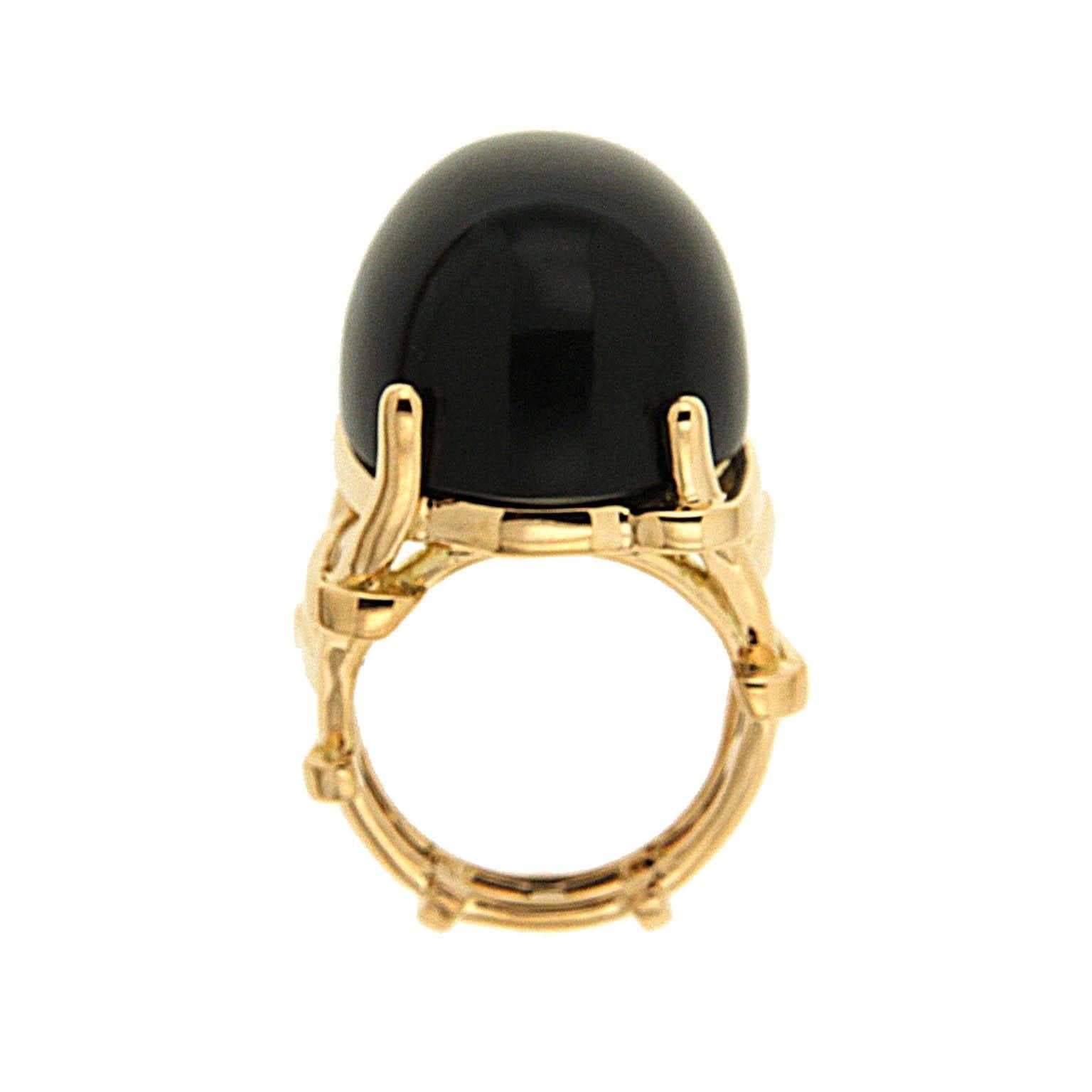 A polished oval cabochon of black jade underlines its gleam. 18k yellow gold round prongs secure the gem. A split shank begins below the prongs in gold strips as they transform into a trellis design. The total weight of the black jade is 56.75