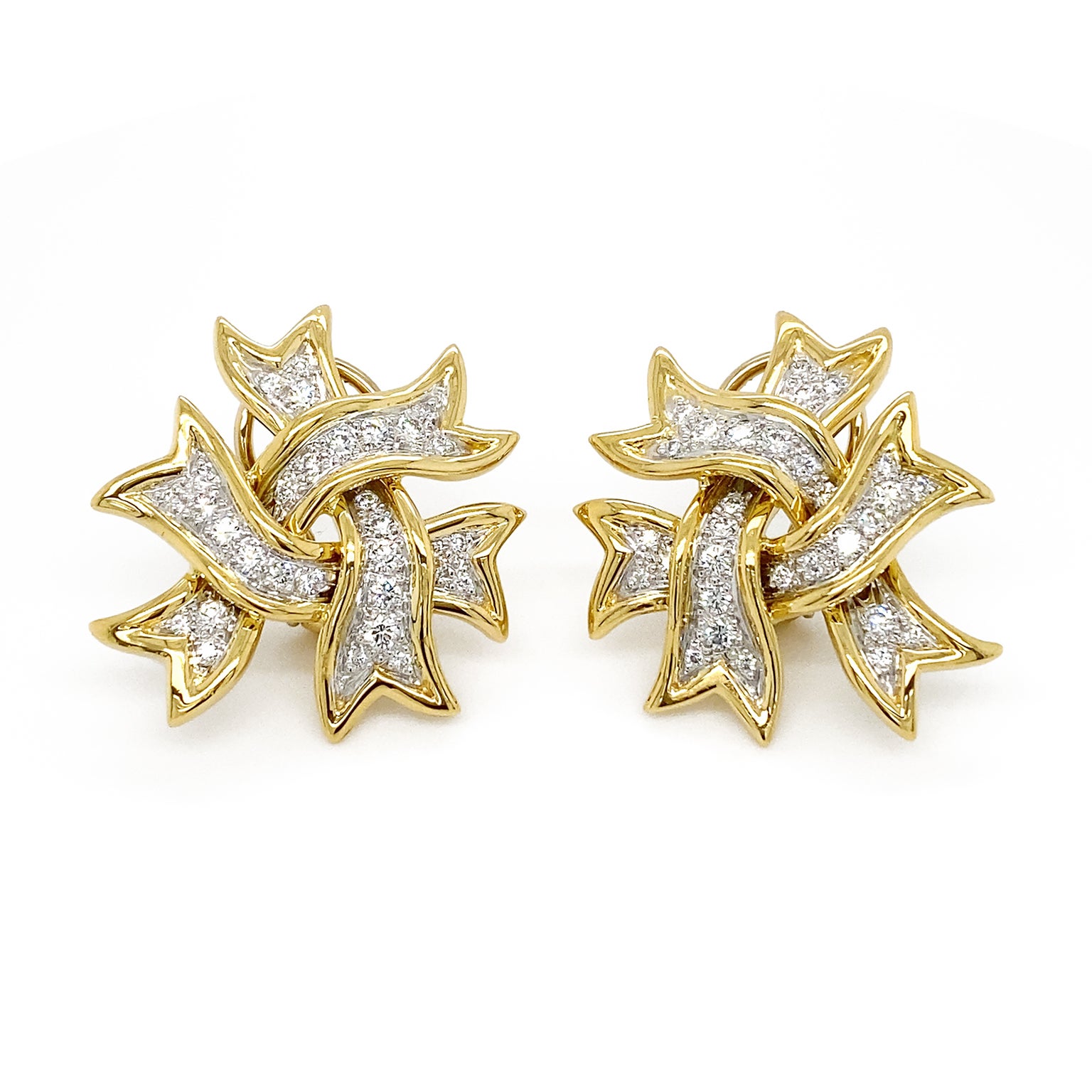 Ribbons bring a festive heart to these earrings. Three 18k yellow gold V-cut ribbons curve to overlay each other. Adorning the center of each ribbon are a row of platinum set brilliant cut diamonds, producing a white flare of light. The total weight