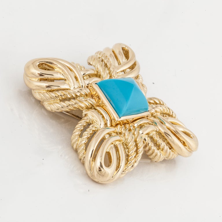 An 18K yellow gold brooch by Valentin Magro, featuring a pyramid shaped turquoise stone in the center.  Beautiful scrolling gold work around the stone.  This brooch measures 2 7/8 inches across, it has a double prong clip closure.  Definitely a