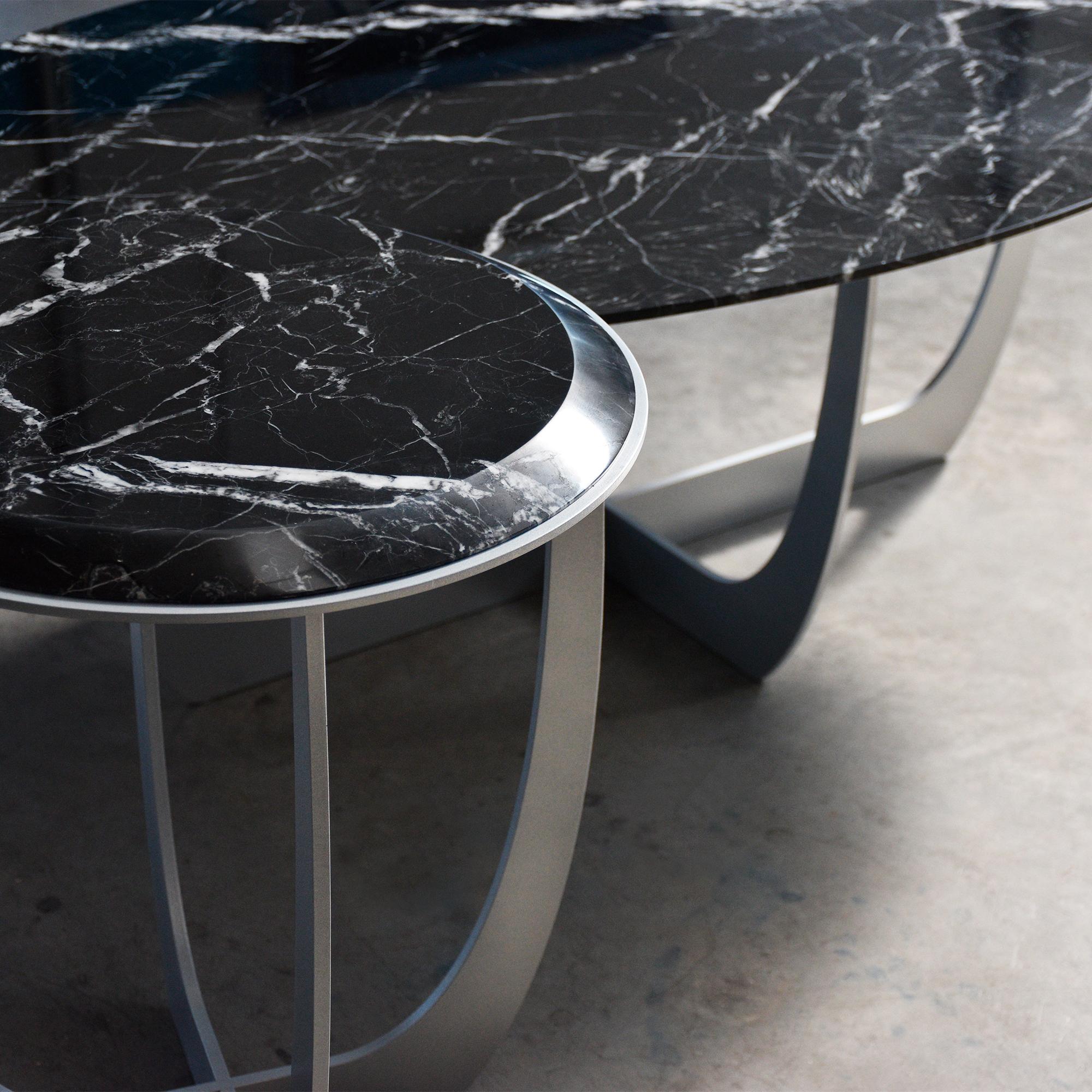 Valentine, un ensemble de tables pour le salon, se caractérise par une base en métal aux formes symétriques et sculpturales, ce qui lui confère une allure contemporaine. 
Le plateau, en marbre naturel, ennobli par le traitement spécial du bord