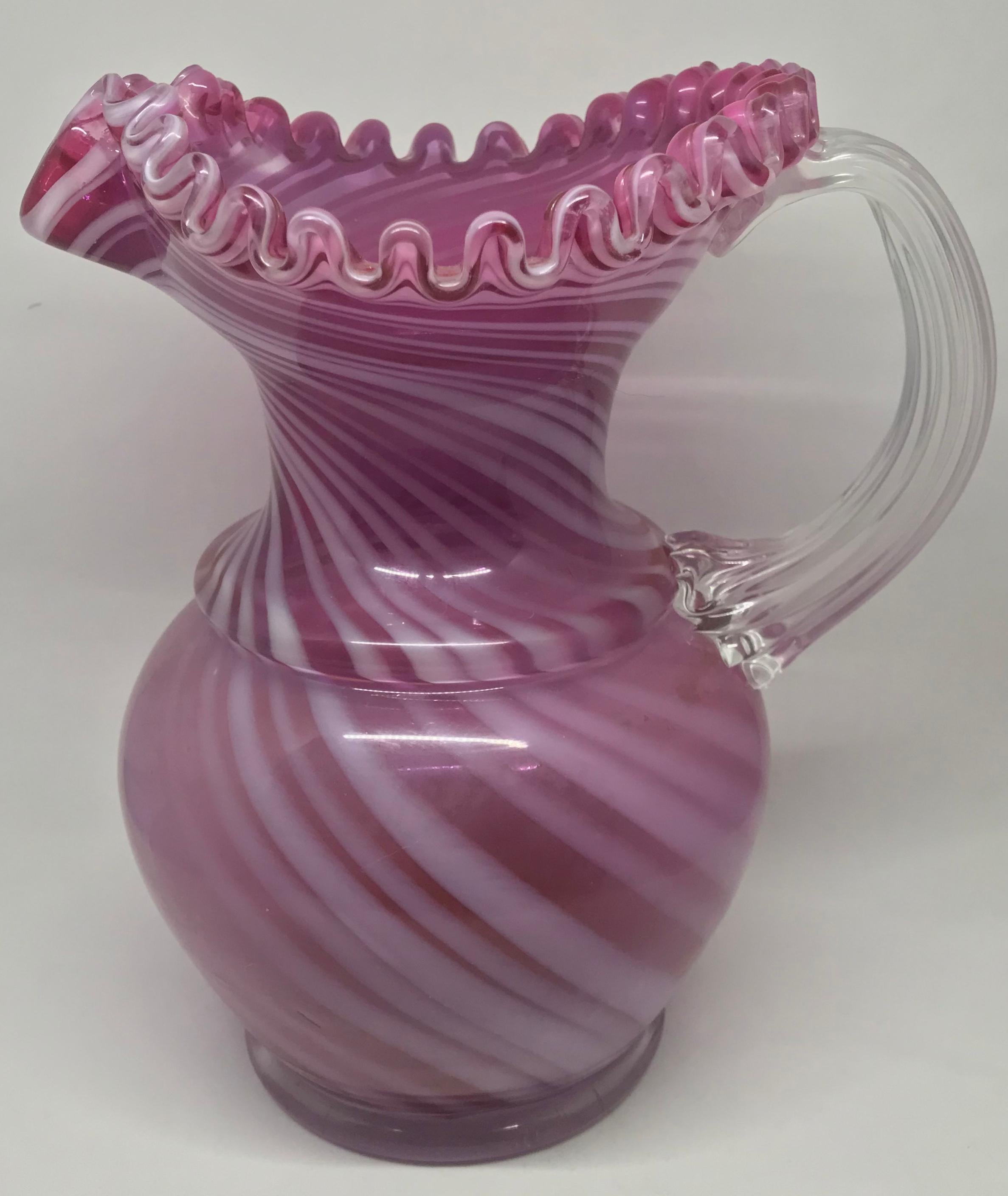 Pink and white striped pitcher. Large American hand blown glass pitcher in rose pink with white striping, ruffled rim and clear glass handle. United States, circa 1900.
Dimensions: 9.5
