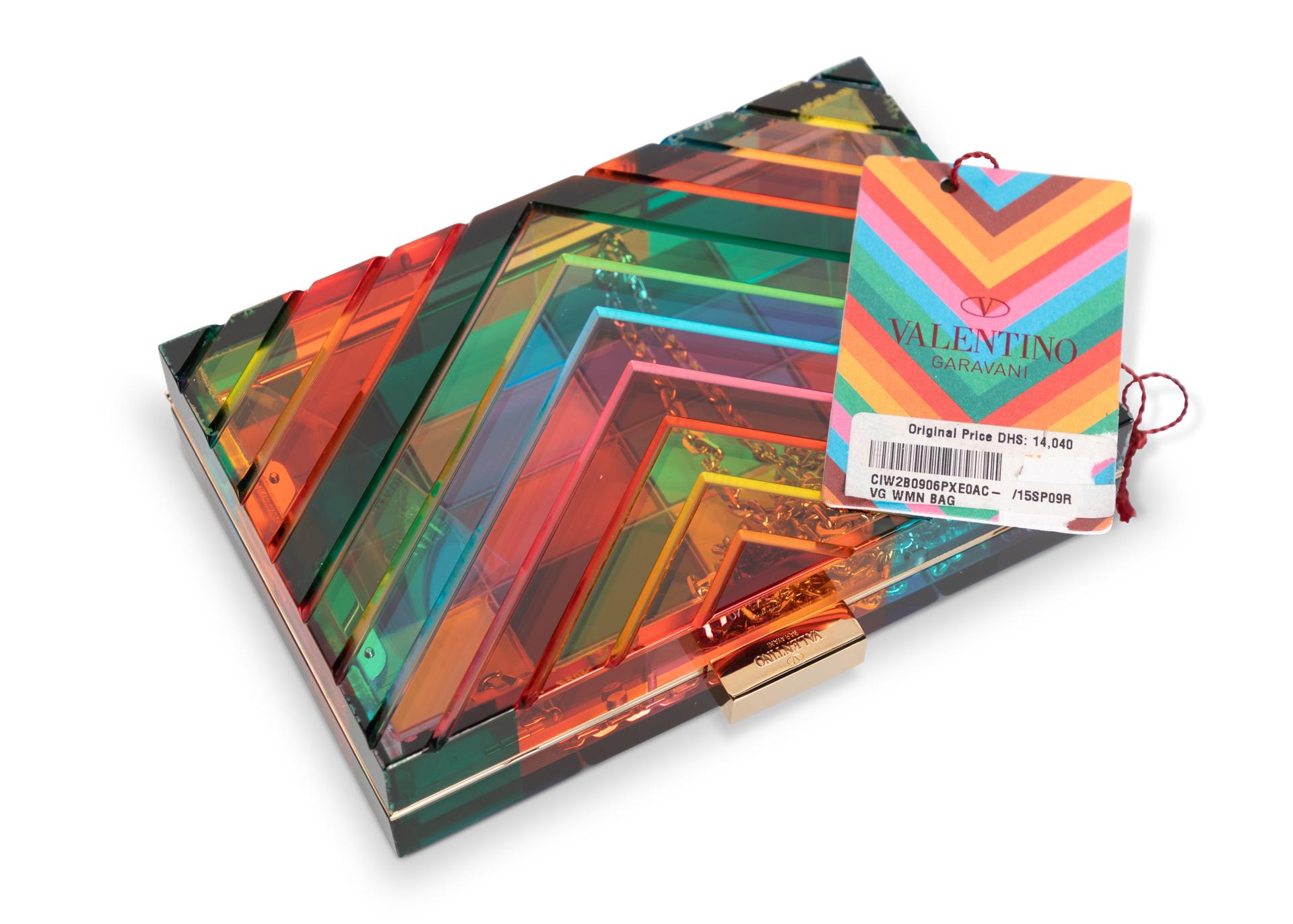 Rainbow acrylic Valentino 1973 minaudière with gold-tone hardware, single detachable gold tone drop-in chain-link shoulder strap, multicolored chevron pattern at front, color block squares pattern on the back. Clear acrylic side vents with the