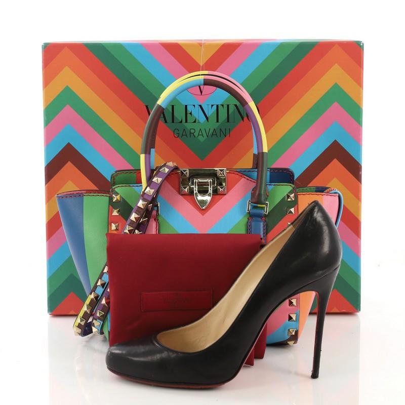 This Valentino 1973 Rockstud Tote Rigid Leather Mini, crafted from multicolor rainbow rigid leather, features dual rolled handles, pyramid stud trim details, and gold-tone hardware. Its clasp lock closure opens to a red leather interior with side