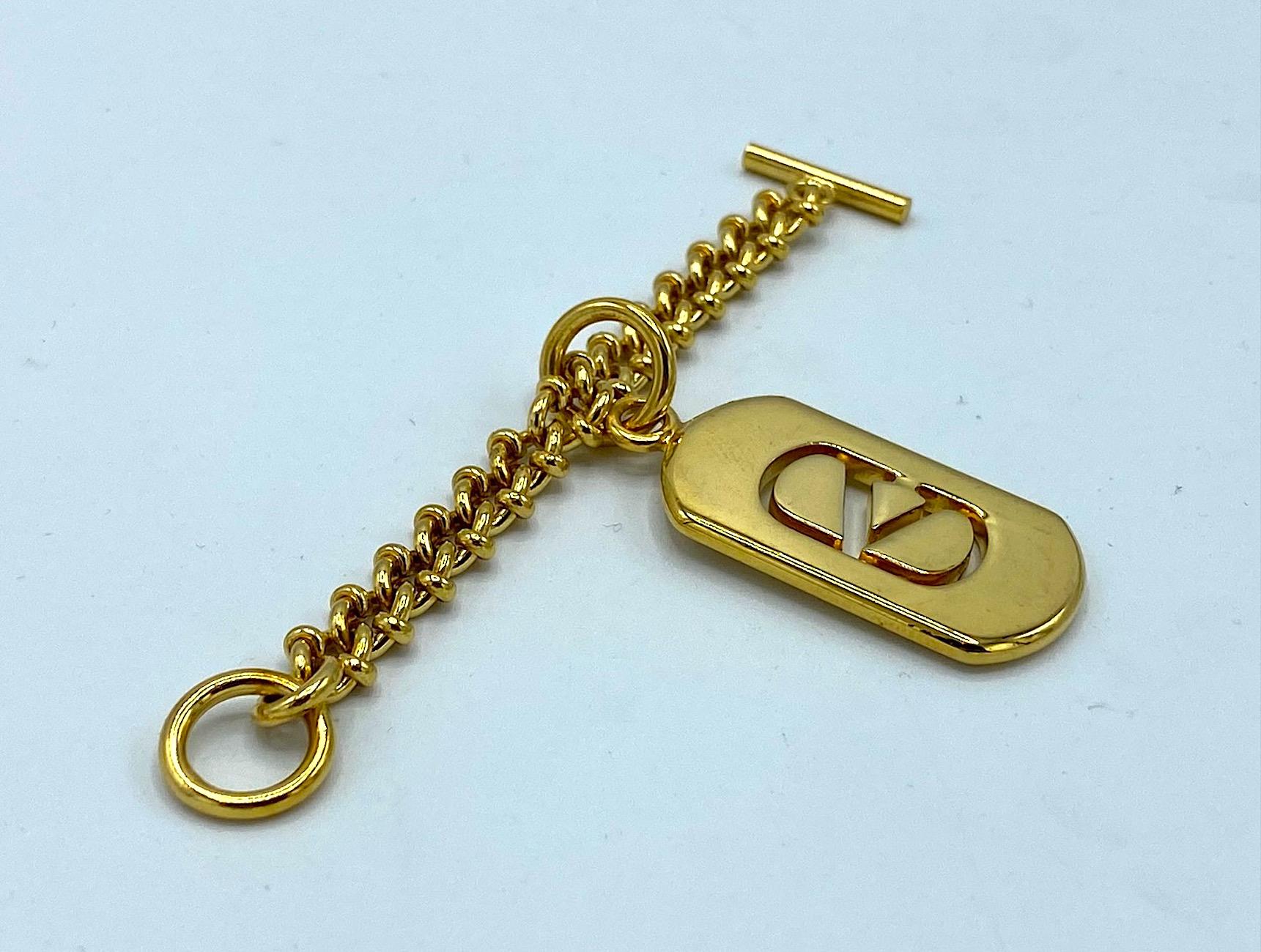A lovely vintage Valentino gold plate key ring with logo dog tag charm. The tag is rectangular with curved ends in shape. The Valentino logo is cut out of the metal. The tag or charm is approximately 0.75  inch wide and 1.5inches long. The chain is